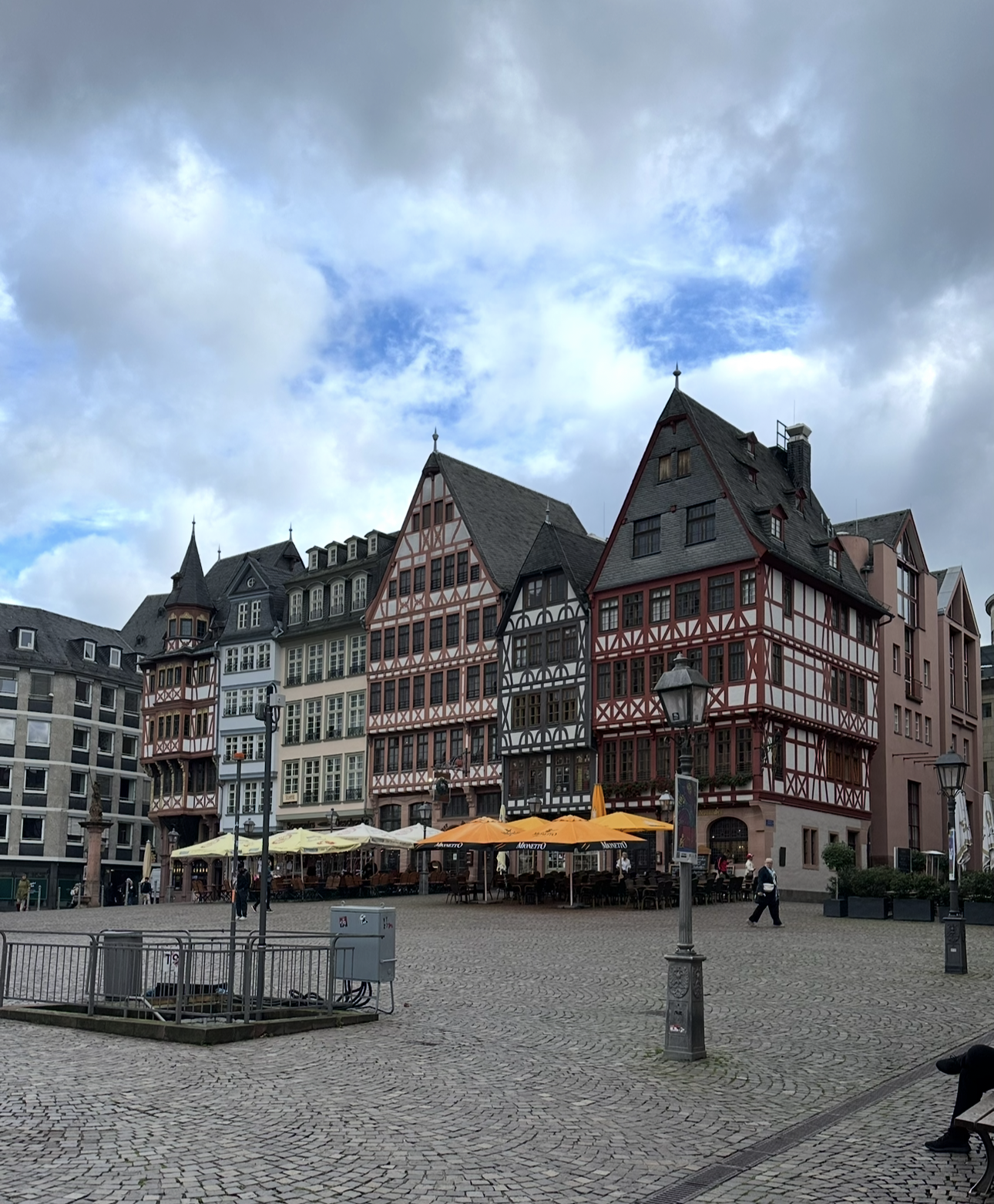 Colorful historic buildings with timber framing in a European town square, outdoor seating with umbrellas, cloudy sky