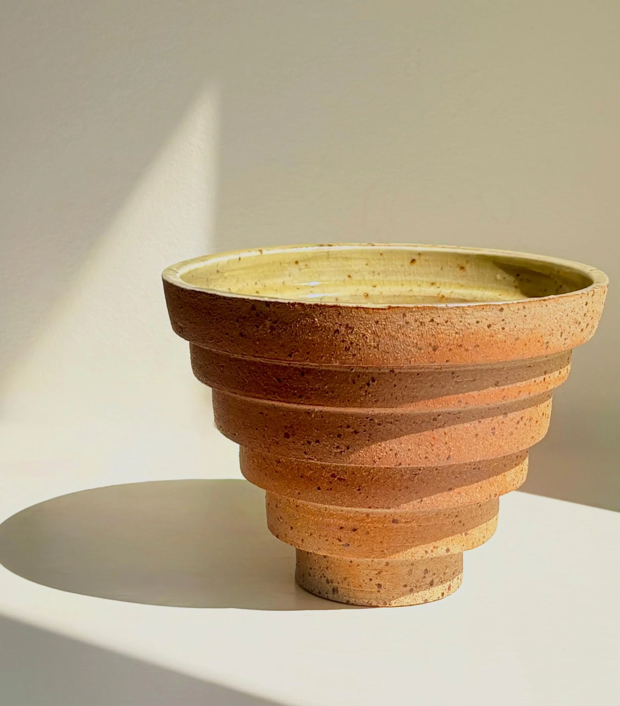 Tiered Earth &ndash; Sculptural Bowl II

Wheel thrown and reduction fired in a gas kiln. Left unglazed on the outside, with a porcelain slip and celadon glaze on the inside. The celadon developed a warm yellow tone during the firing, which was a love