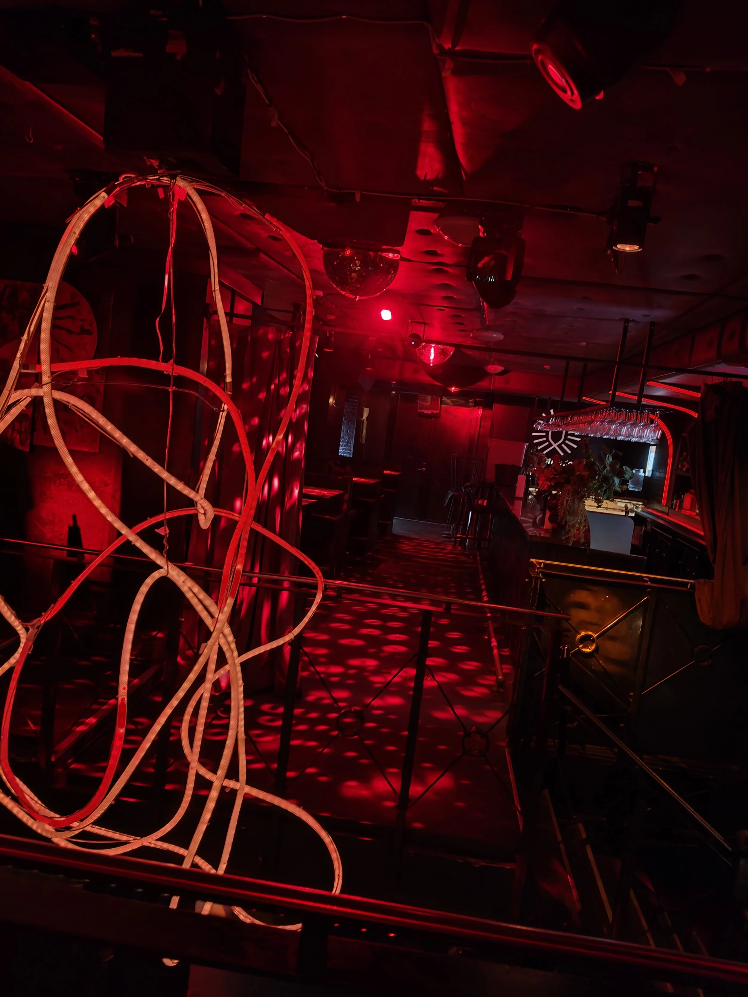 Eksempel på NatDance natklub med rødt lys, neonbelysning, ophængte glas og abstrakte metalskulpturer på væggene.