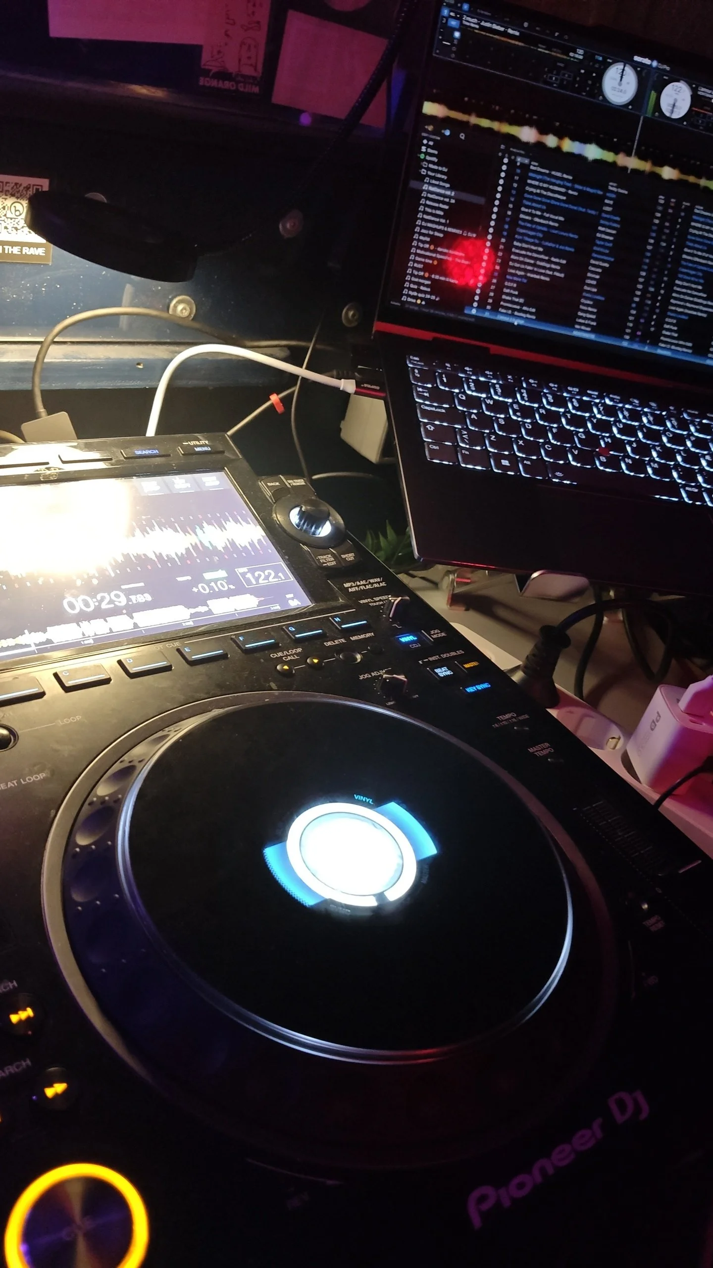 Nærbillede af DJ-udstyr, herunder en pladespiller, en laptop med musiksoftware og en digital mixer, i en dæmpet belysning.