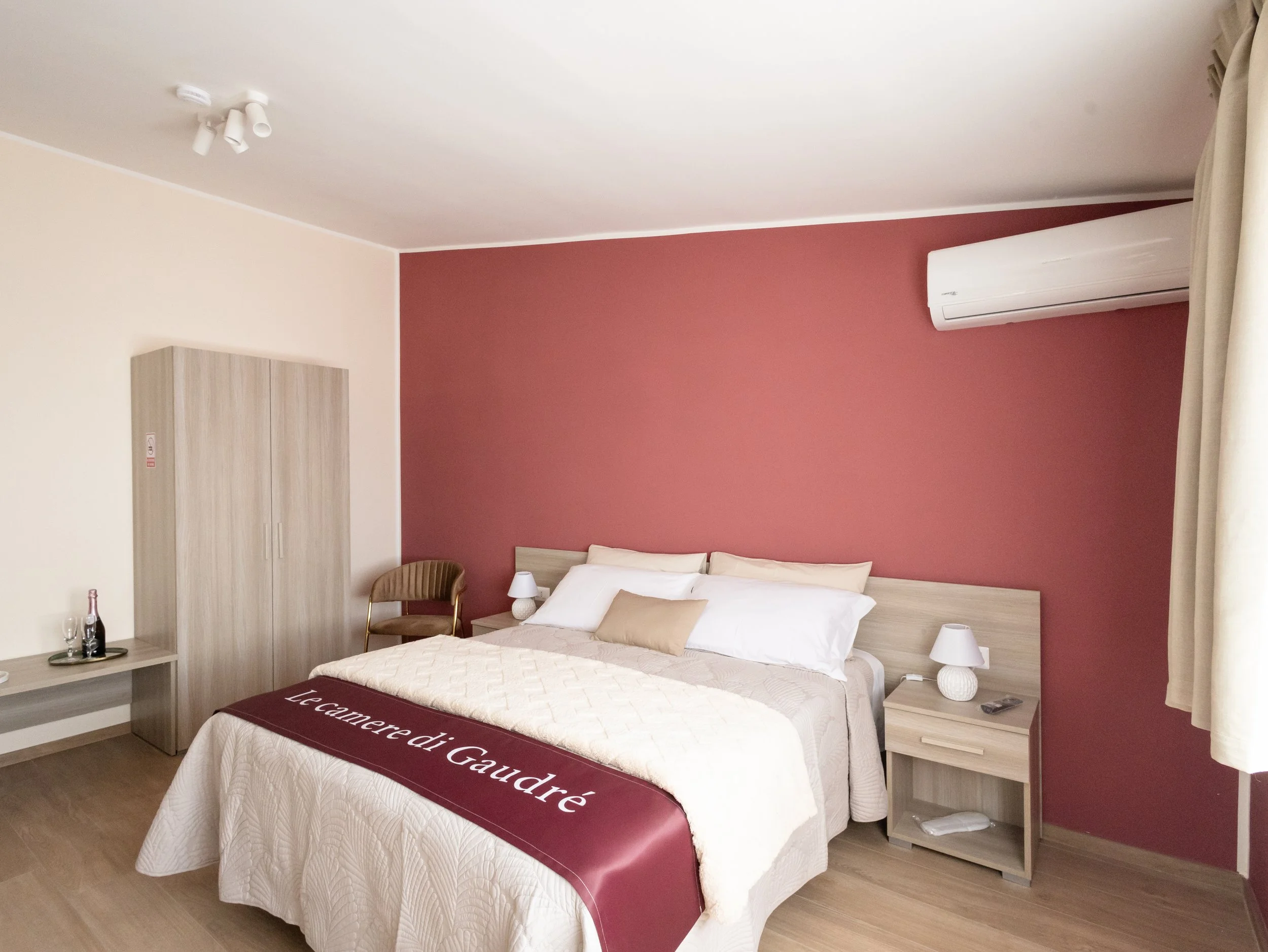 Camera da letto con pareti rosa e beige, letto con copriletto bianco, specchio e comodini con lampade