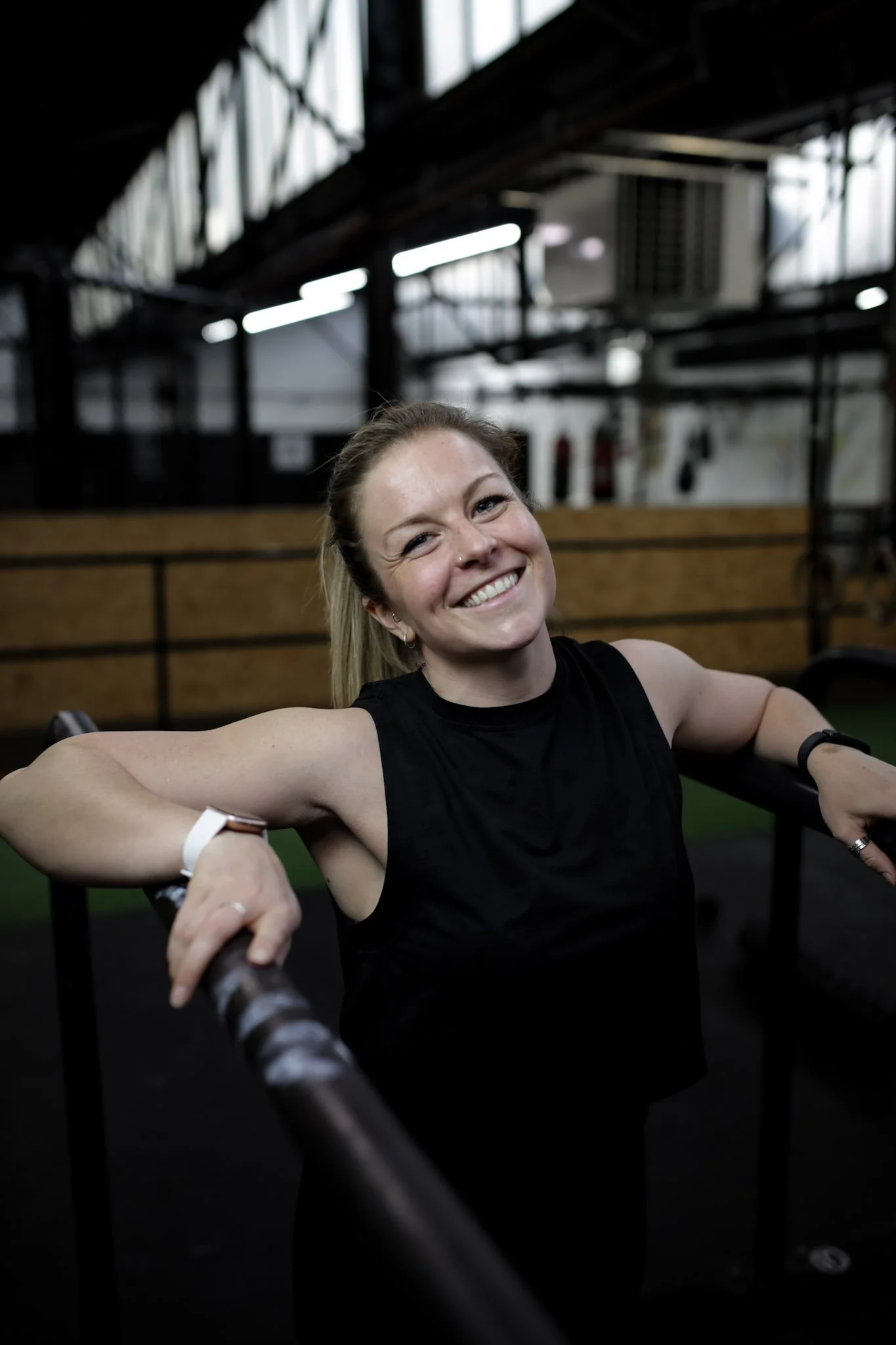 The coach at Your Project Me is smiling and leaning on parallel bars in a gym.