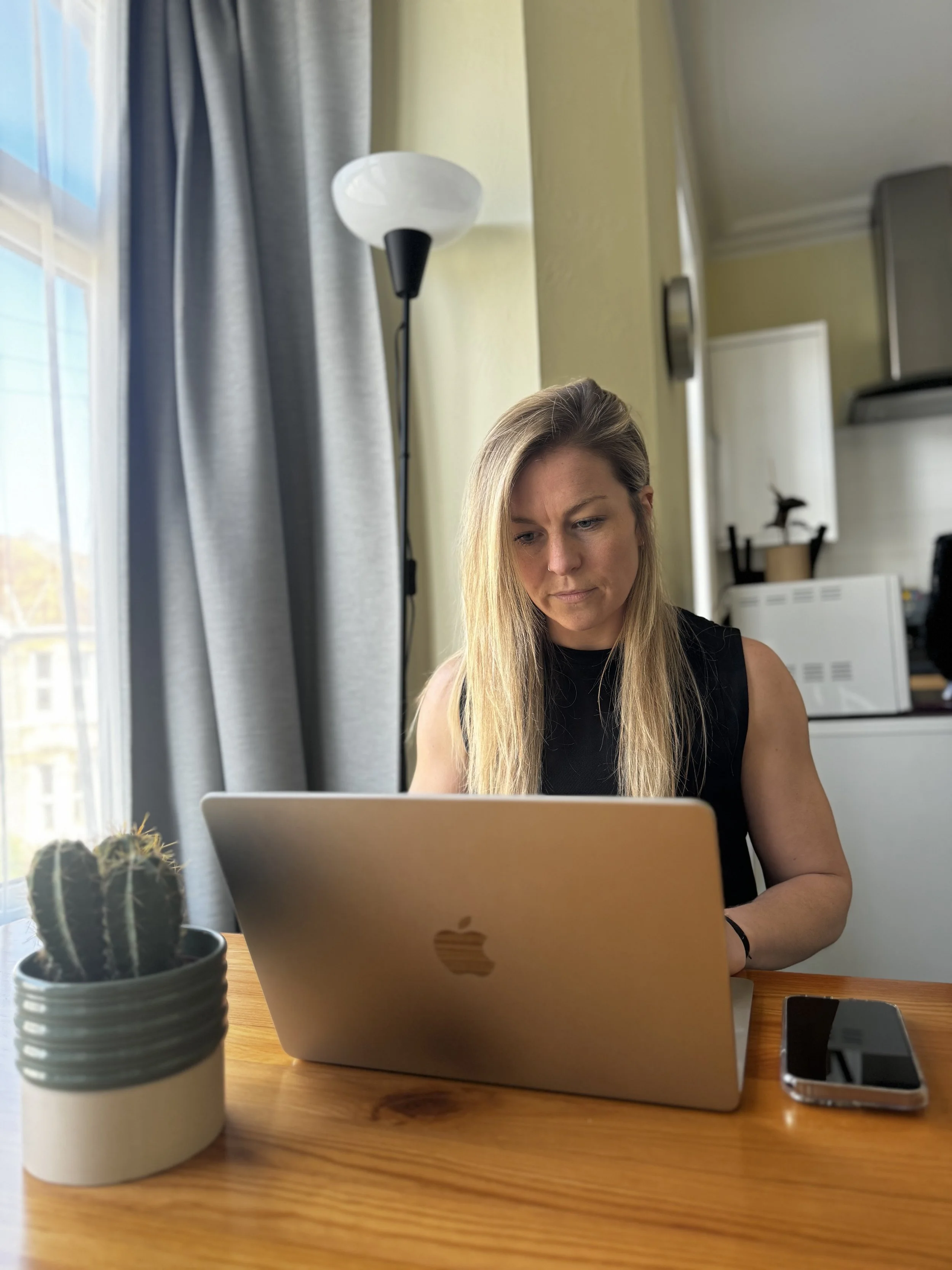A female online coachworking on a laptop at home performing online check-ins with her clients.