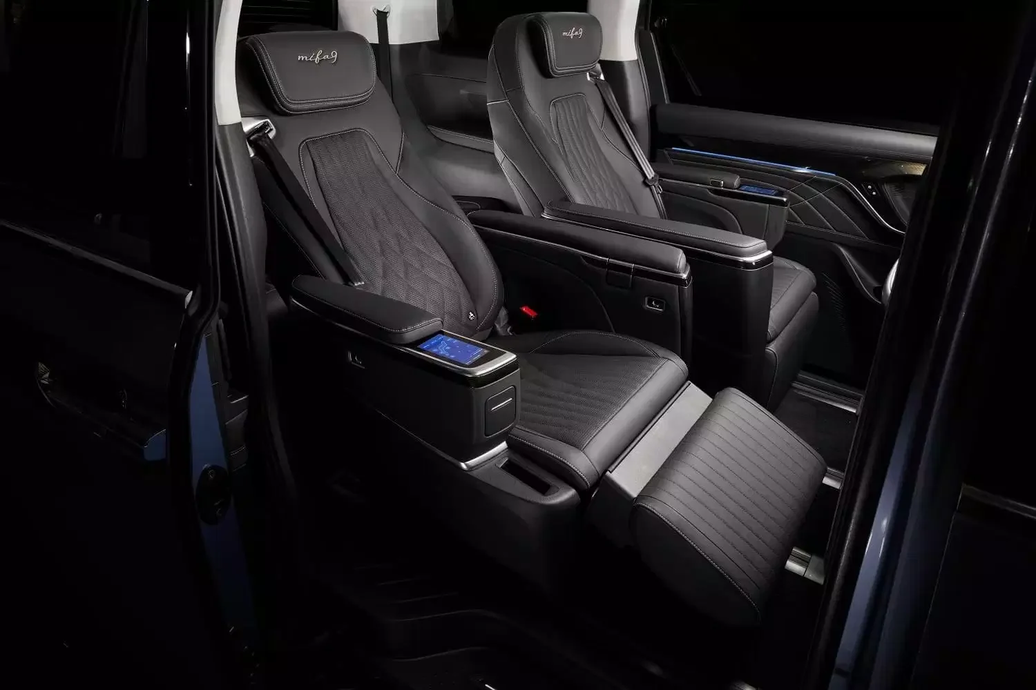 Luxury car interior with two black leather seats, control panels, and armrests.