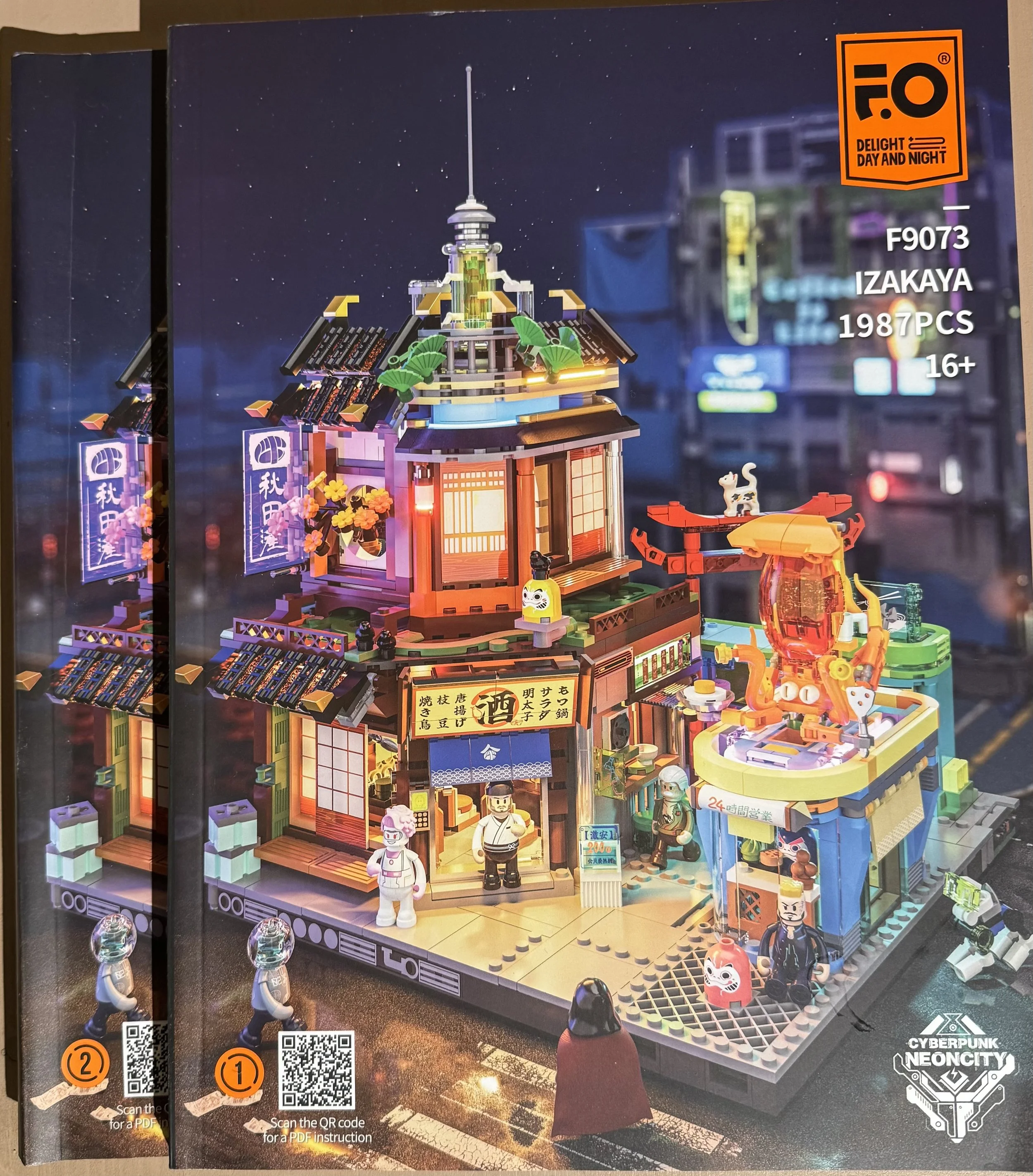 Une maquette de bâtiment en LEGO représentant une scène urbaine la nuit, avec des personnages, des enseignes en japonais, et un décor cybernétique, portant la mention 'Cyberpunk Neoncitiy'.