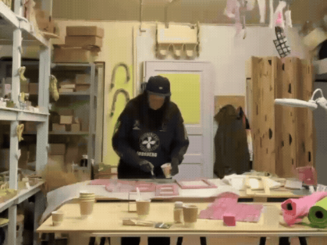 Person working on crafting pink and white foam board projects in a workshop with shelves, wood pieces, and craft materials.