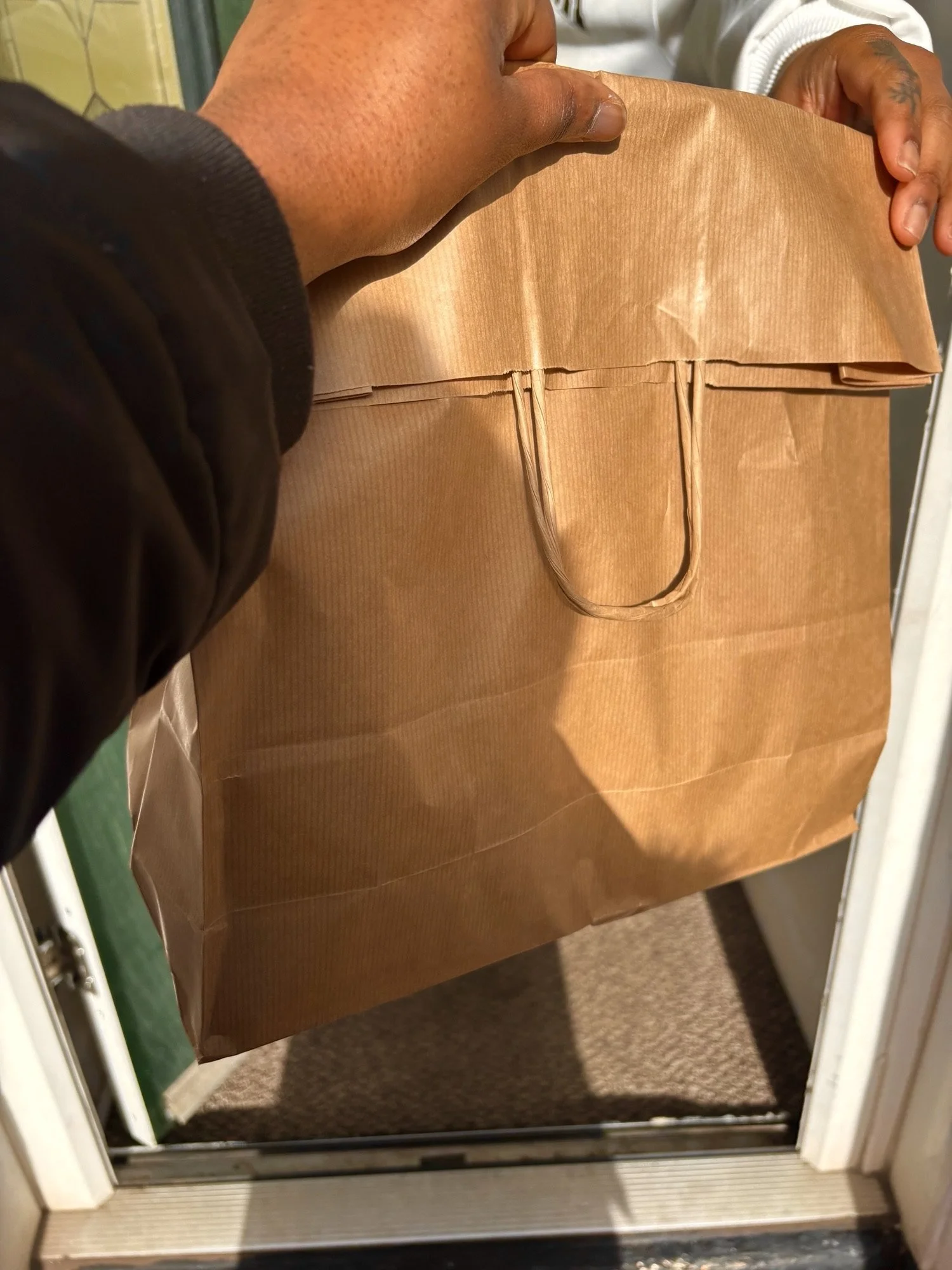 Person holding a brown paper grocery bag in front of a door.