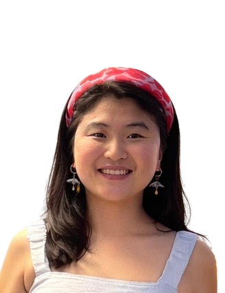 A young woman with long dark hair wearing a red and white patterned headband, smiling, dressed in a white top, with earrings.