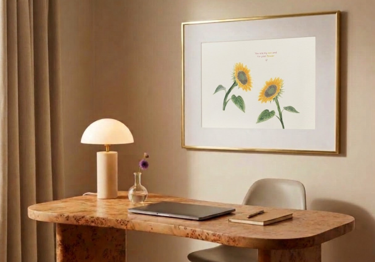 A cozy corner with a wooden table, a white lamp, a small vase with a purple flower, a closed laptop, a notebook, and a pen. A framed sunflower print hangs on the wall.