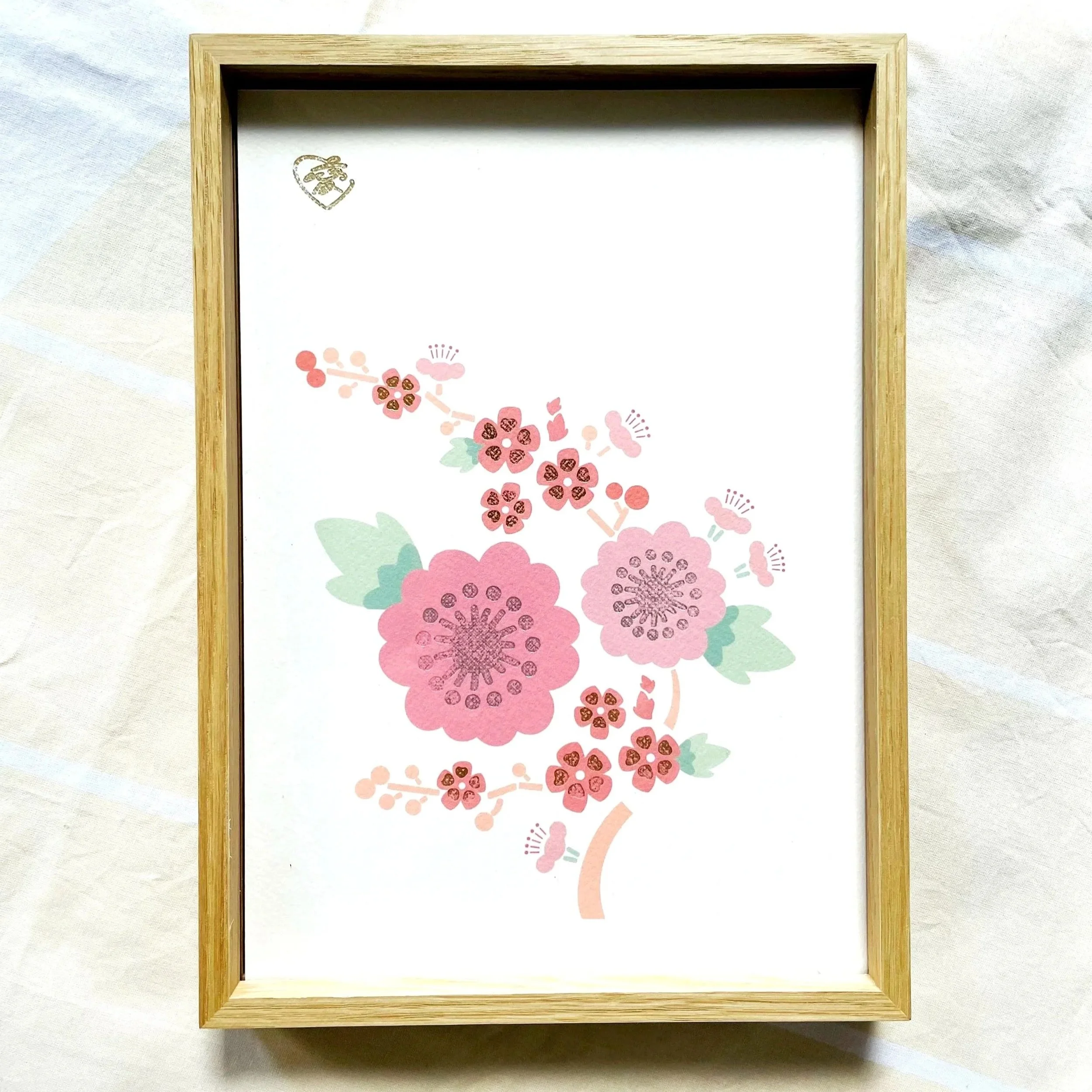 A floral illustration of pink cherry blossoms with green leaves, set in a wooden frame.