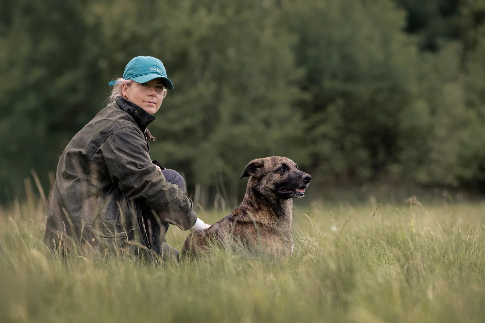 Frau in Jacke und Mütze mit braunem Hund im Grünen