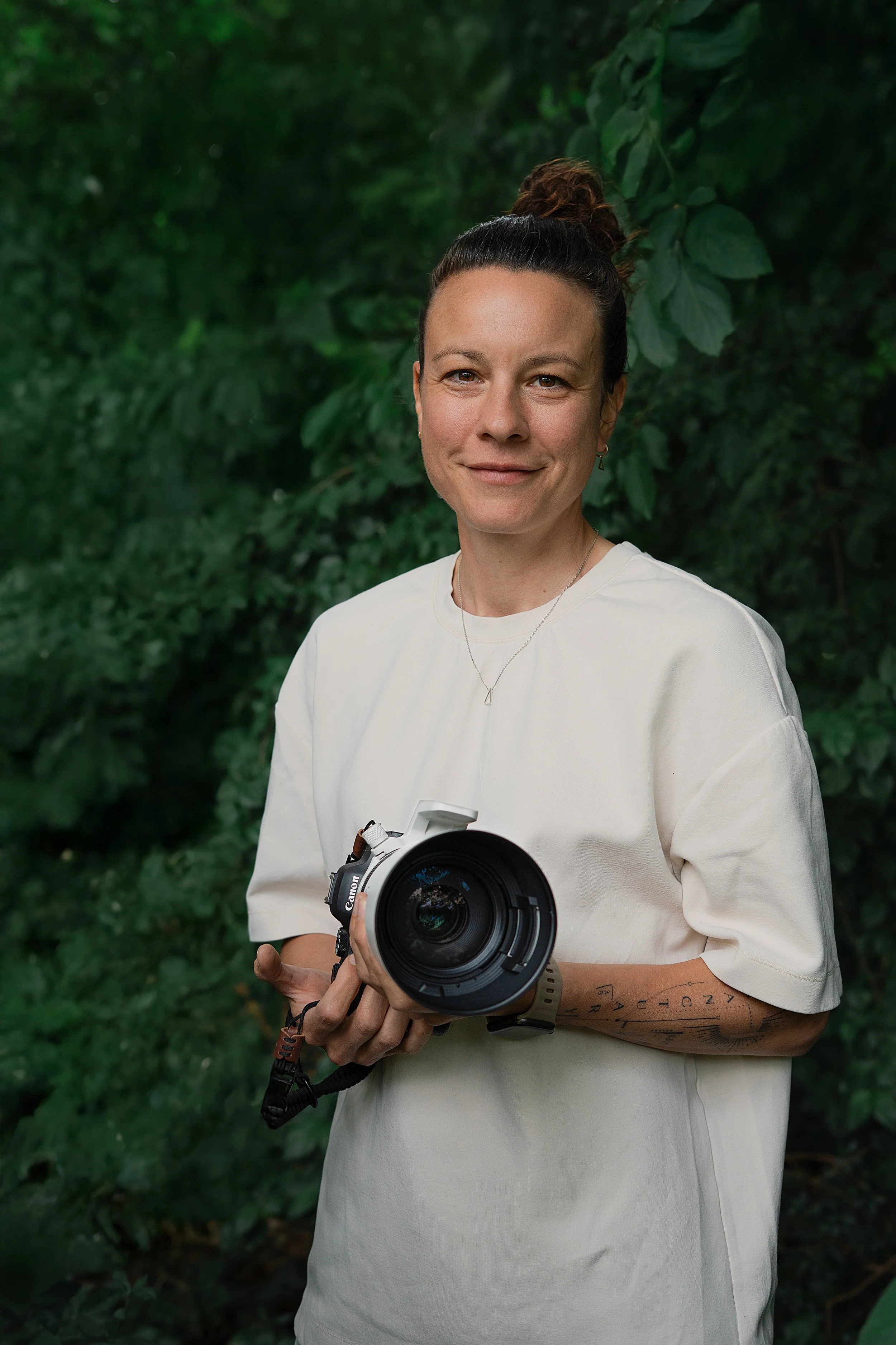 Eine Frau hält eine professionelle Kamera vor grünem Blätterdach im Freien