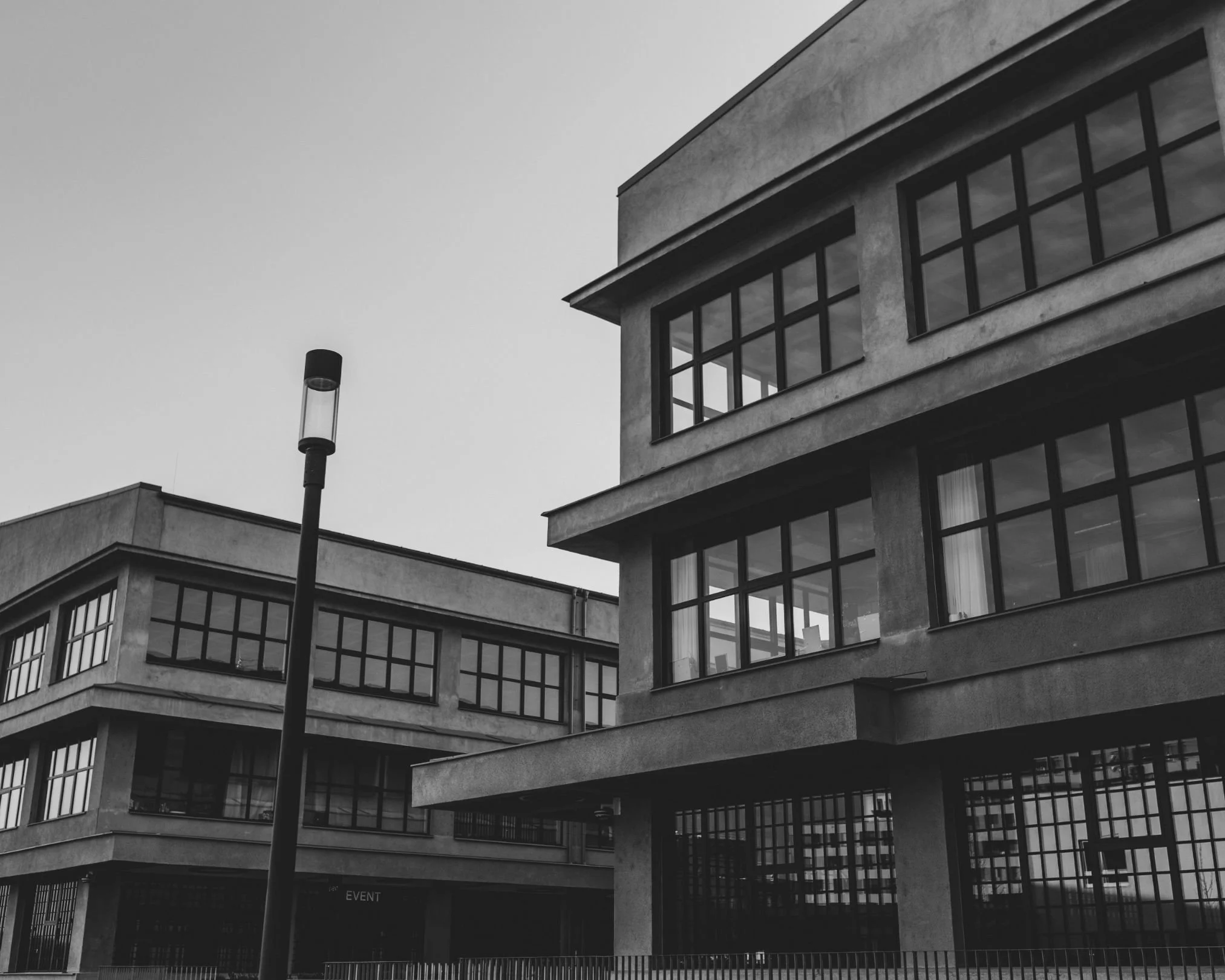 Black and white photo of modern multi-story buildings with large glass windows and a streetlamp in the foreground.