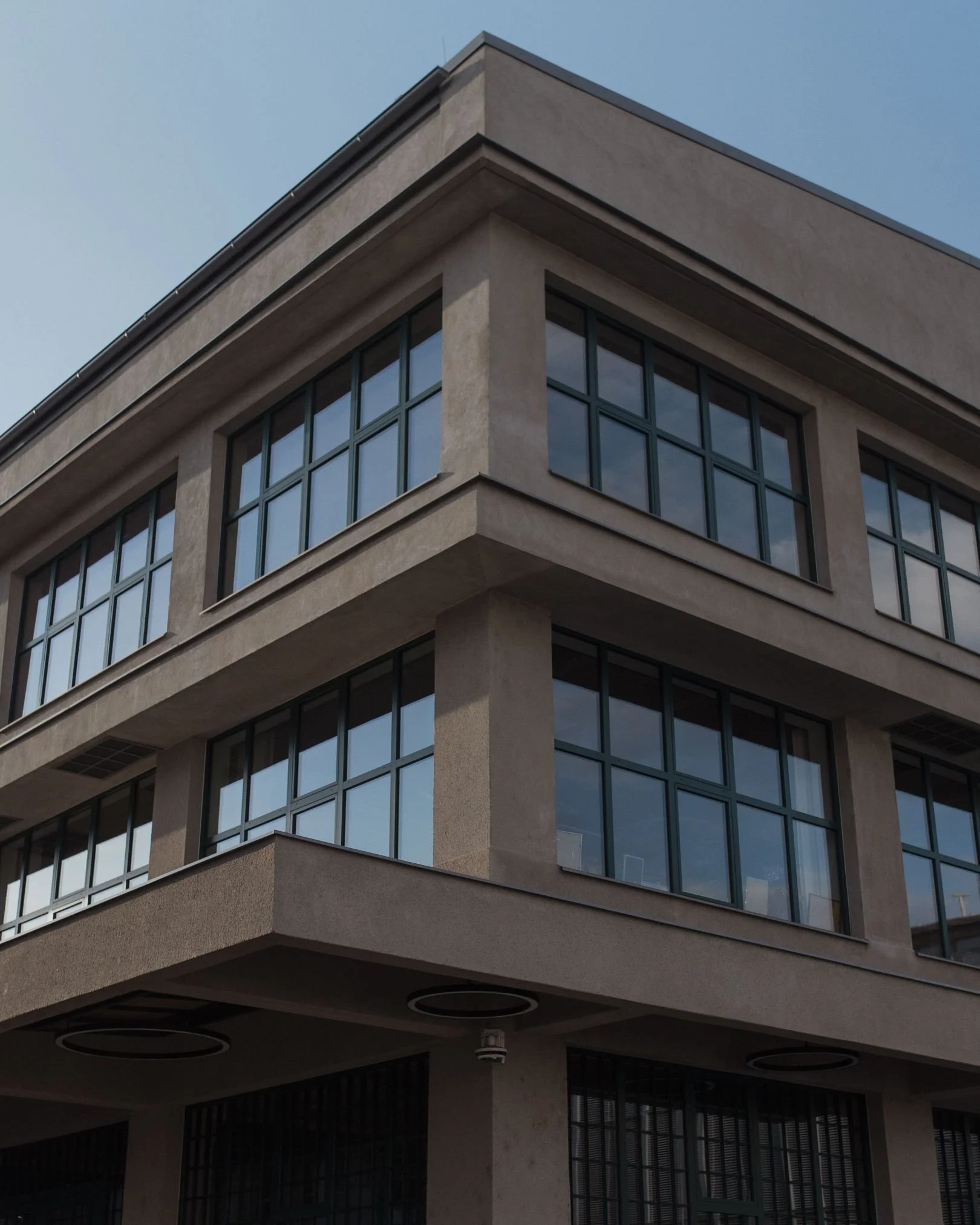 A modern multi-story building with large glass windows and concrete walls, featuring a corner with visible floors and ceiling details, under a clear blue sky.