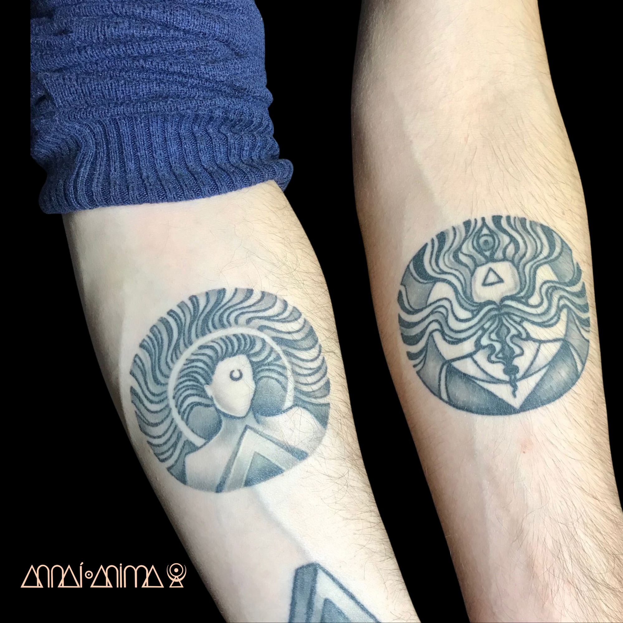 Two forearms with black and gray tattoos, one on each arm, featuring abstract, wavy line designs. The person on the left is wearing a blue sleeve, and the background is black.
