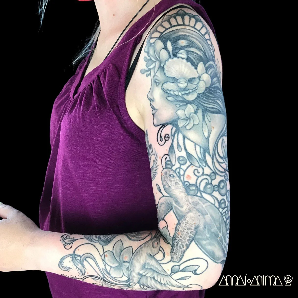 Tattoo of a woman with floral and oceanic elements on her upper arm.