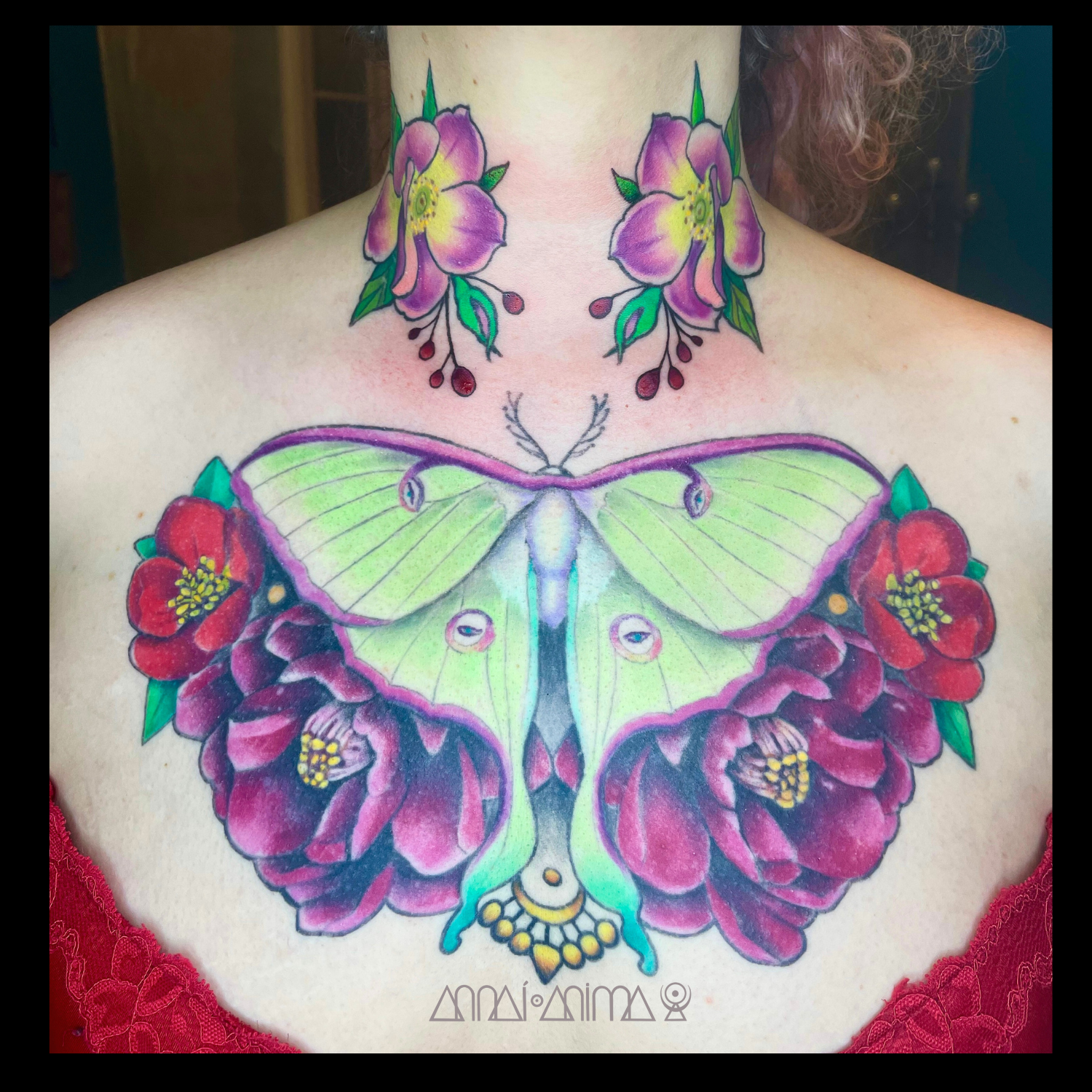 Colorful tattoo of a large butterfly with green and purple wings, surrounded by red flowers on a person’s chest and neck.