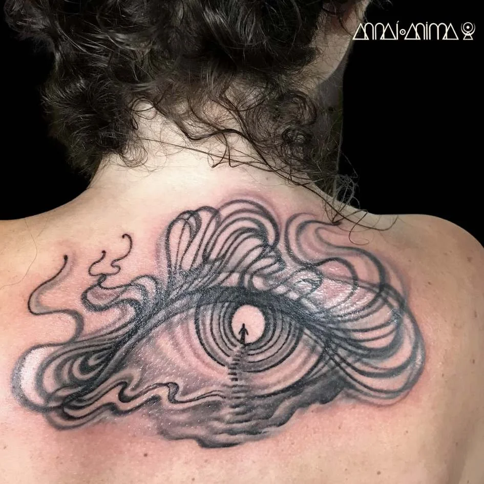 A tattoo of an eye with concentric circles and swirling lines on a person's upper back.