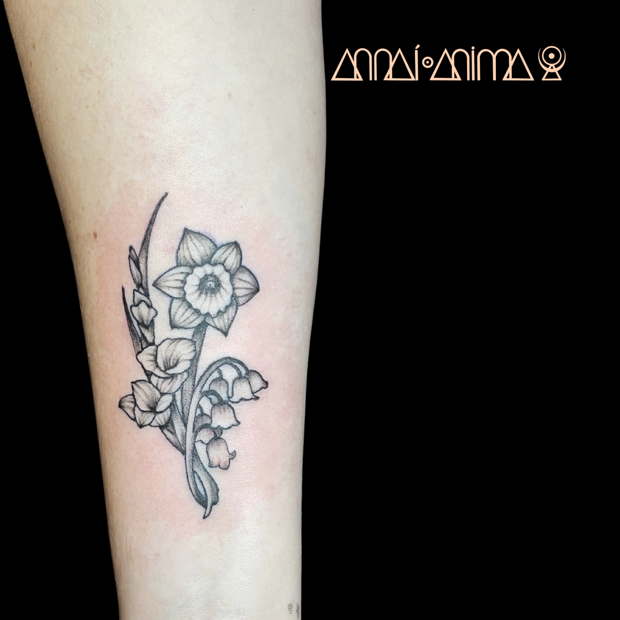 Black and gray floral tattoo on a person's arm featuring a daffodil with smaller flowers and leaves.