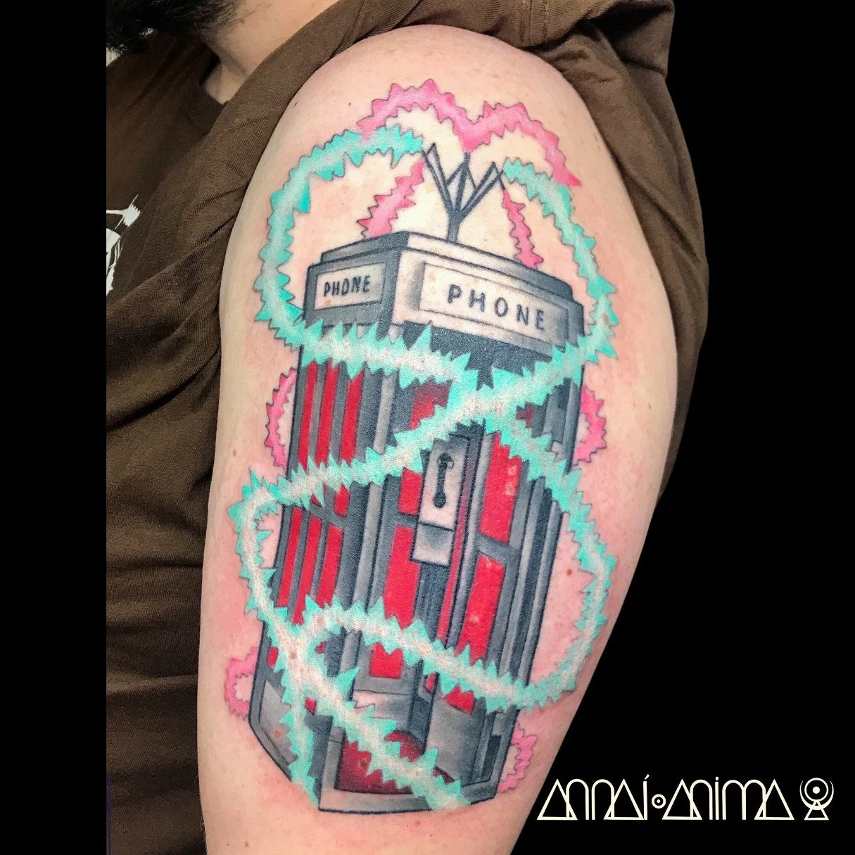 Colorful tattoo of a vintage payphone with a heart-shaped outline in pink, teal, and purple, on a person's arm.