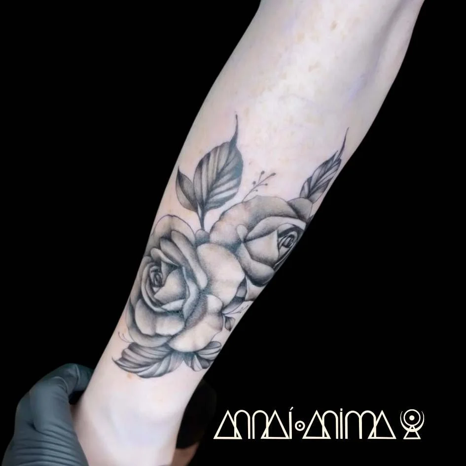 Black and gray tattoo of a bouquet of roses and leaves on a person's forearm.