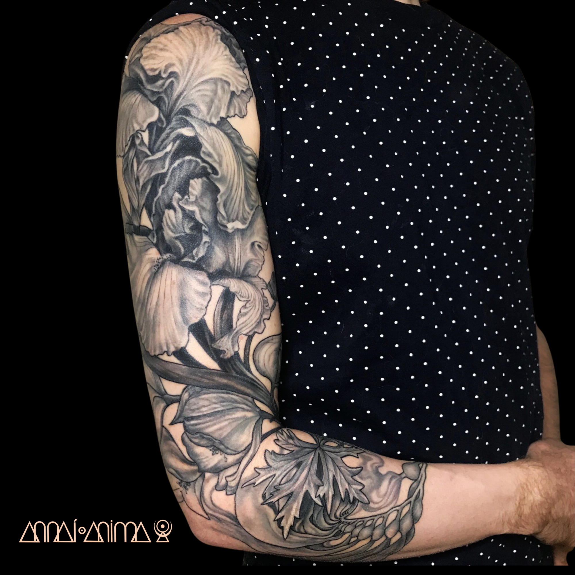Close-up of a person's arm with a detailed black and gray floral tattoo featuring lilies and leaves.