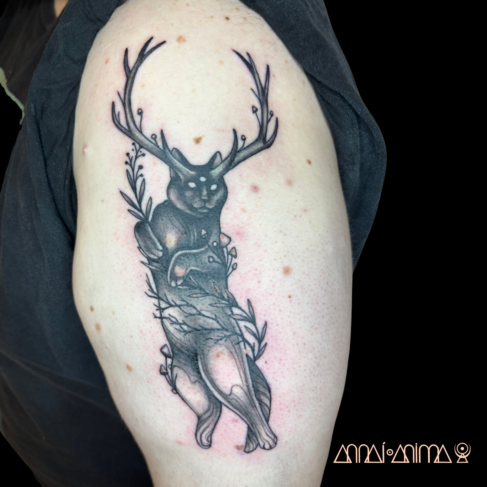 Black tattoo of a surreal animal with a deer-like head and antlers, a body combining a cat and bear, holding a sword, surrounded by leaves.