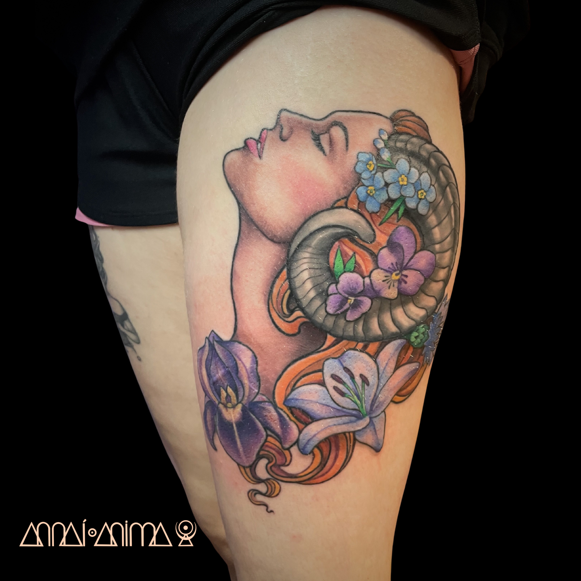 A tattoo of a woman with closed eyes and flowing hair, surrounded by purple and blue flowers, including lilies and pansies, on a person's upper thigh.