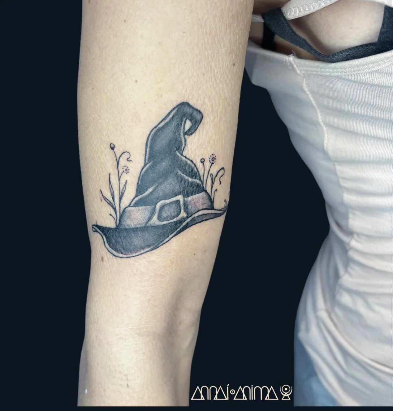 Tattoo of a dinosaur skeleton wearing a Santa hat, surrounded by small floral sketches on the person's forearm.