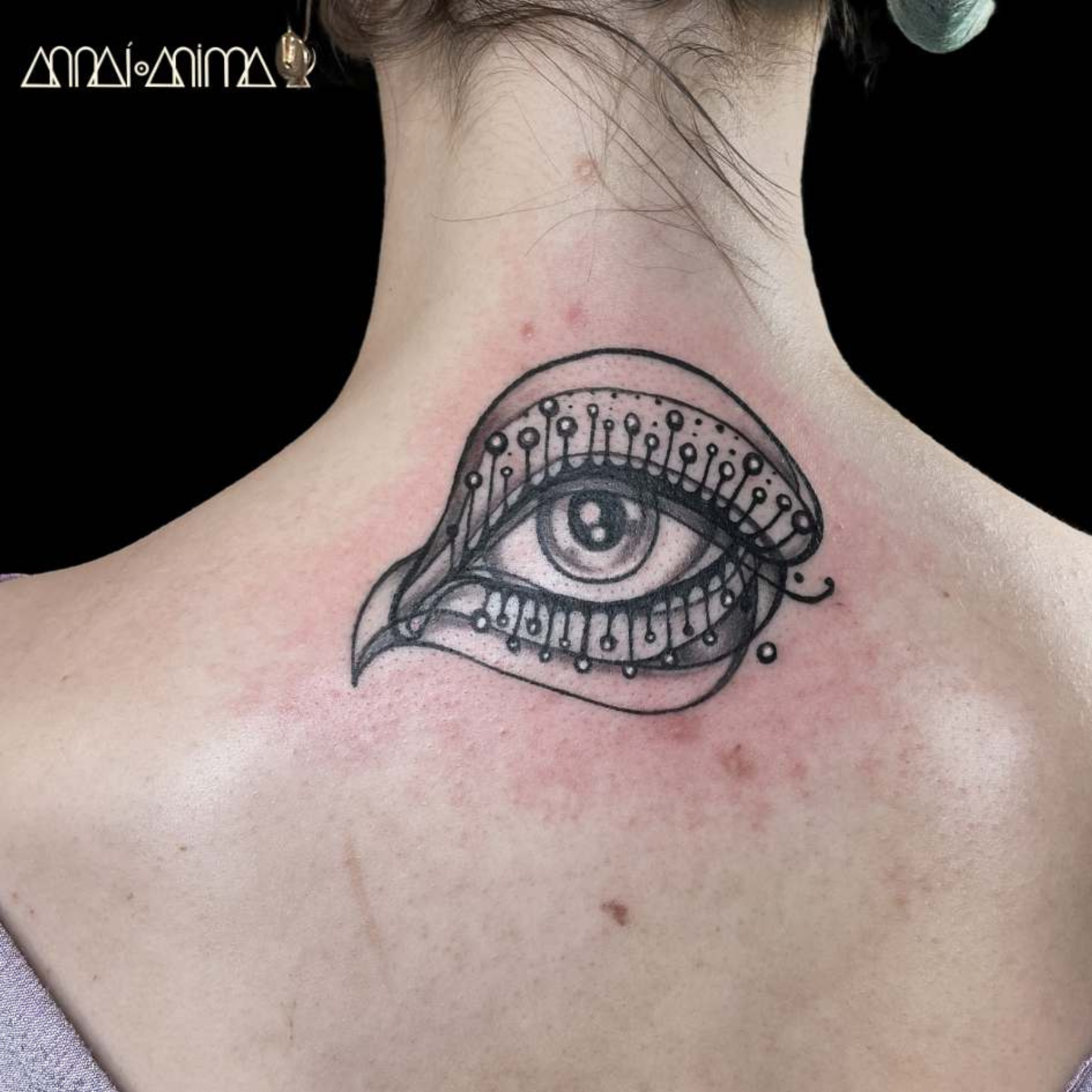 Tattoo of an eye with ornate decorative details around it on a person's neck.