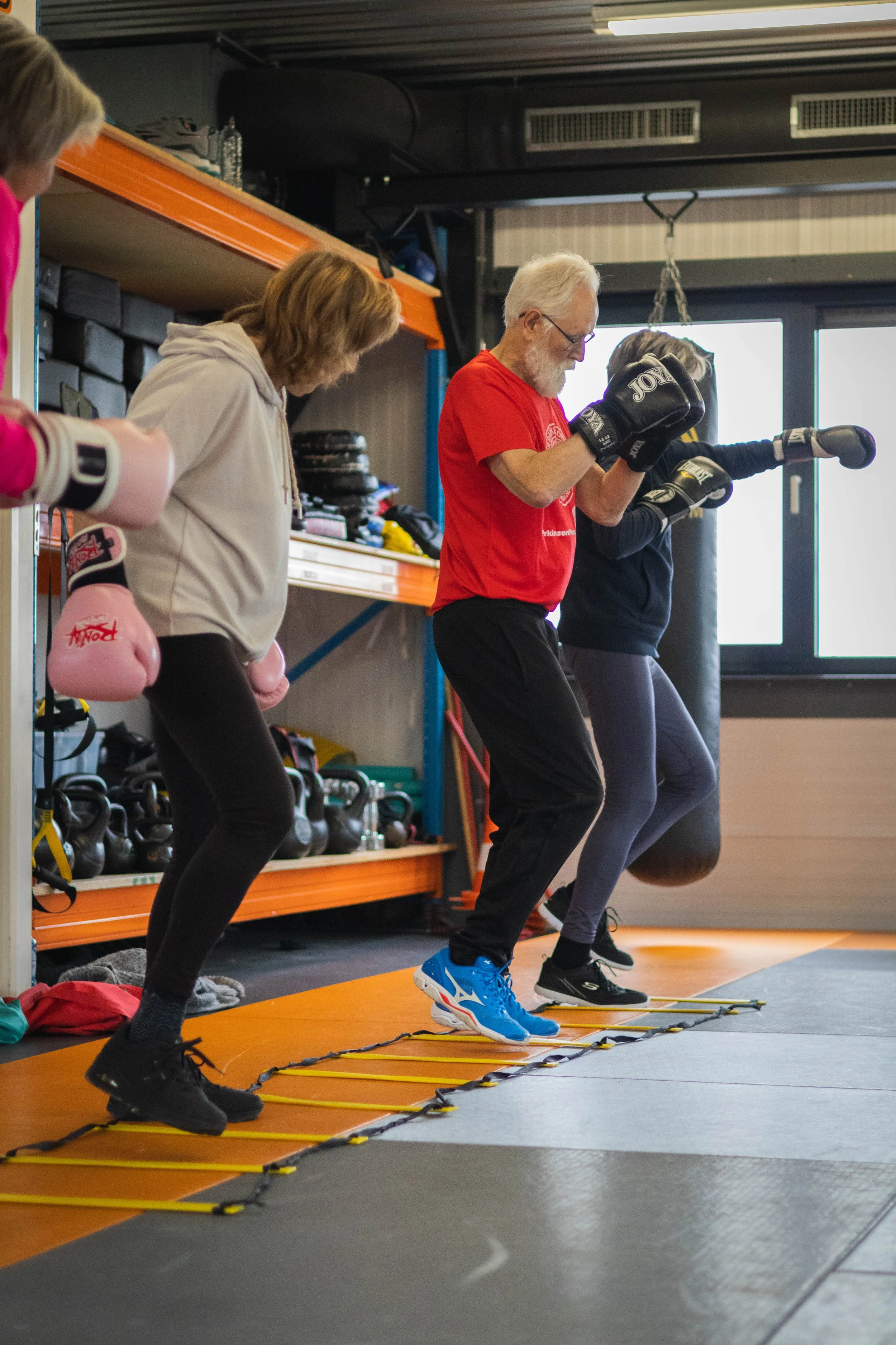 Vijf personen die aan een fitness of bokstraining deelnemen, met stappen en bokshandschoenen, in een sportschool.