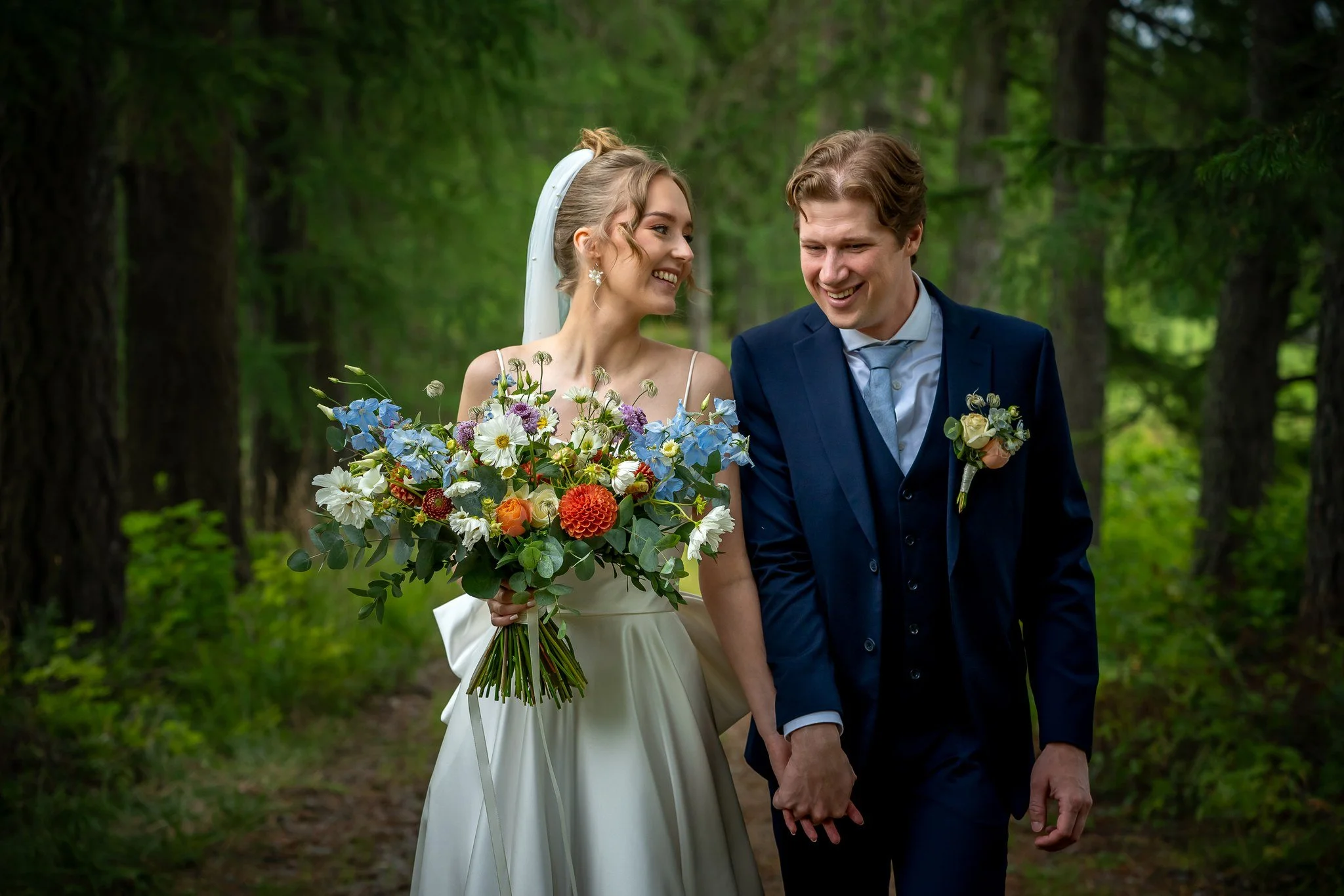 Hääparin kävely metsässä, nainen pitää suurta kukkakimppua ja mies hymyilee.