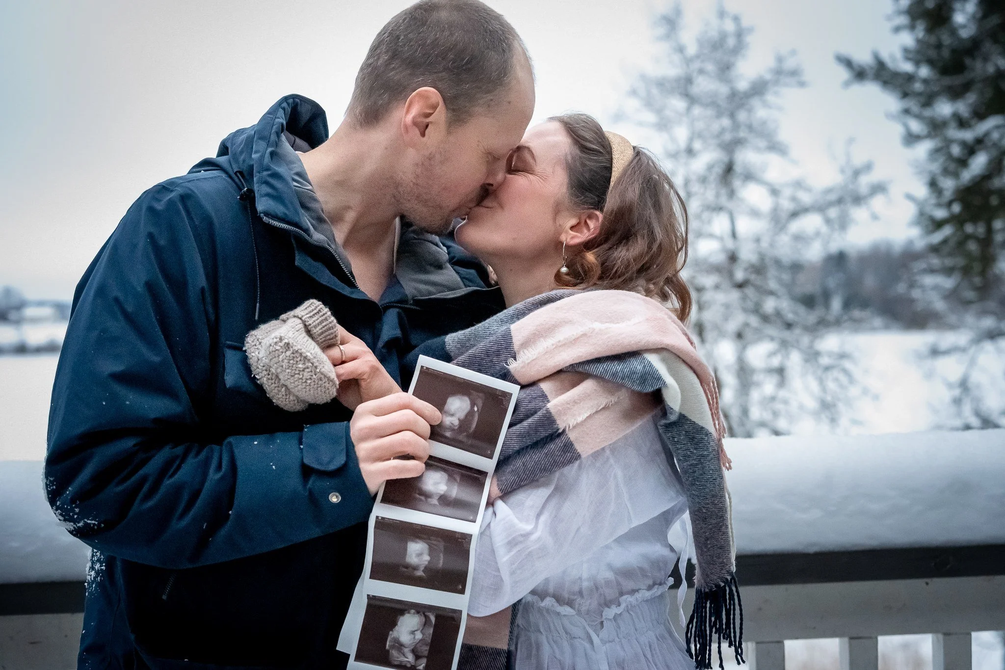 Rakas pari suutelee toisiaan ulkona, toinen heistä pitää ultraäänikuvaa kädessään, taustalla luminen maisema.
