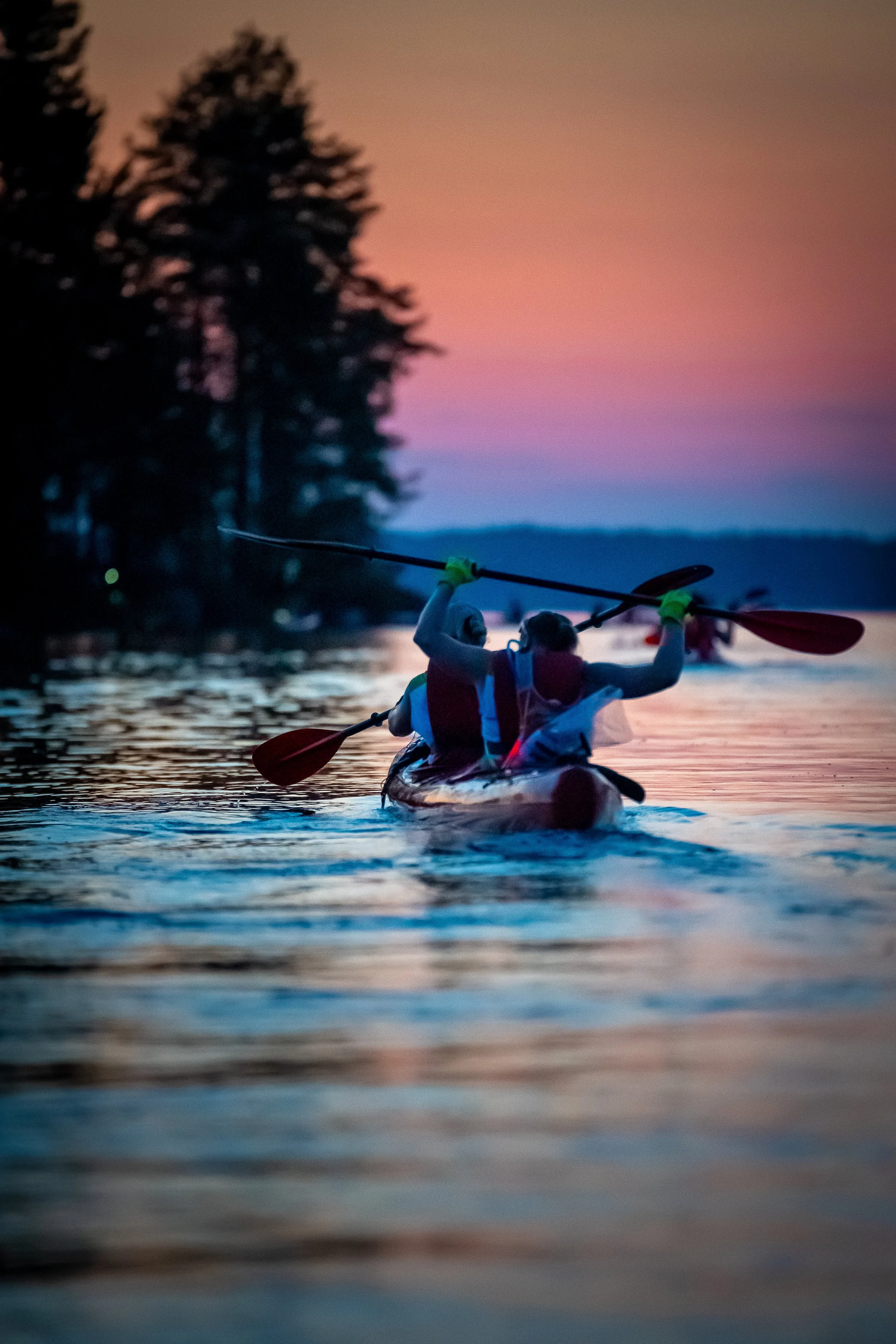 Rakentava kajakki vesillä auringon laskun aikaan, taustalla puita ja värikäs taivas.