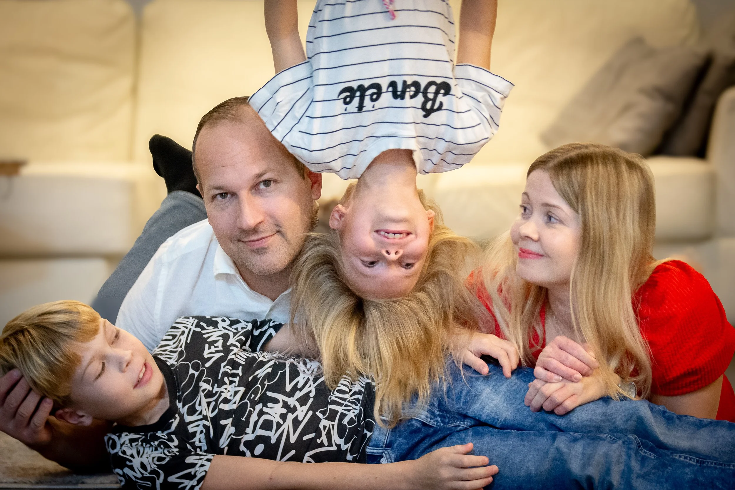 Perhe leikkii lattialla kotona, lapset ja vanhemmat iloisia.