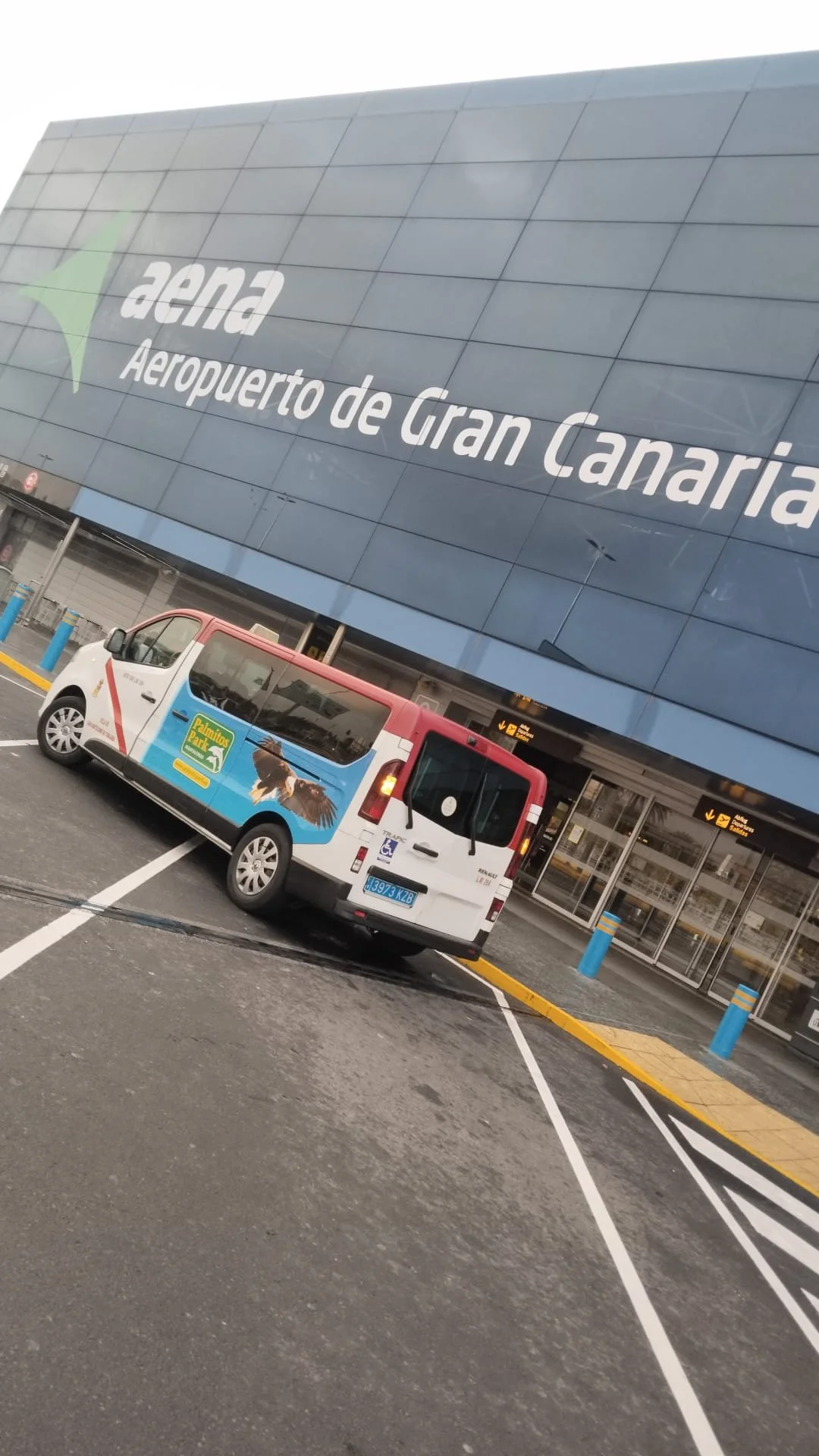 Entrada principal del Aeropuerto de Gran Canaria con un vehículo de transporte en el estacionamiento.