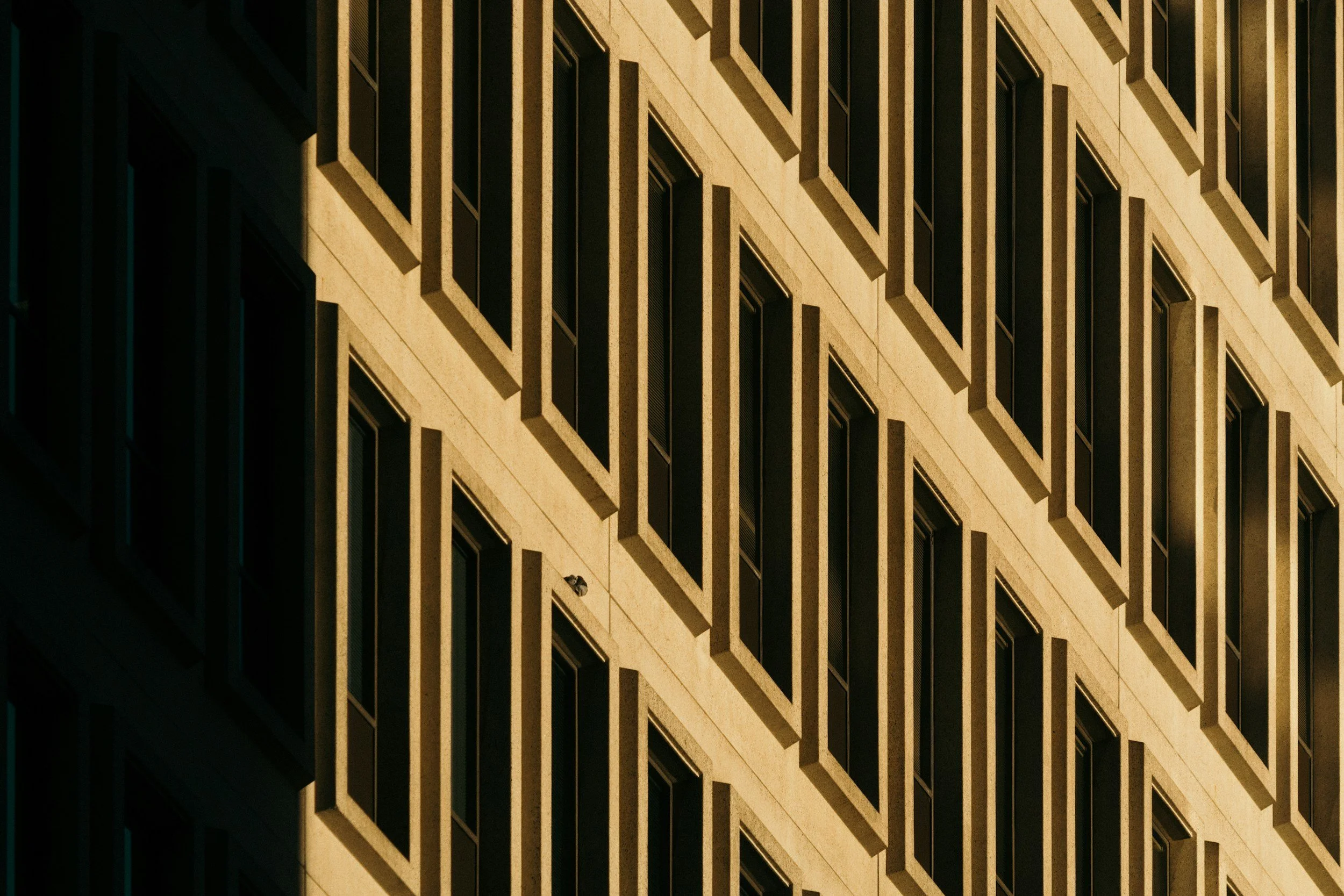 Close-up view of a modern building with a grid-like facade featuring multiple rows of windows with deep, protruding frames, during daytime.
