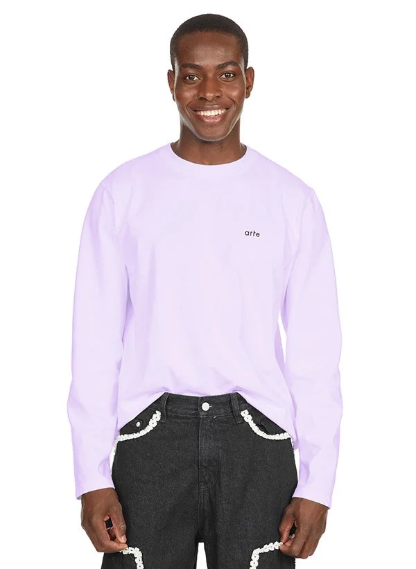 Une personne souriante portant un t-shirt blanc avec le mot 'arte' écrit dessus, et un pantalon noir avec des détails en chaîne blanche.