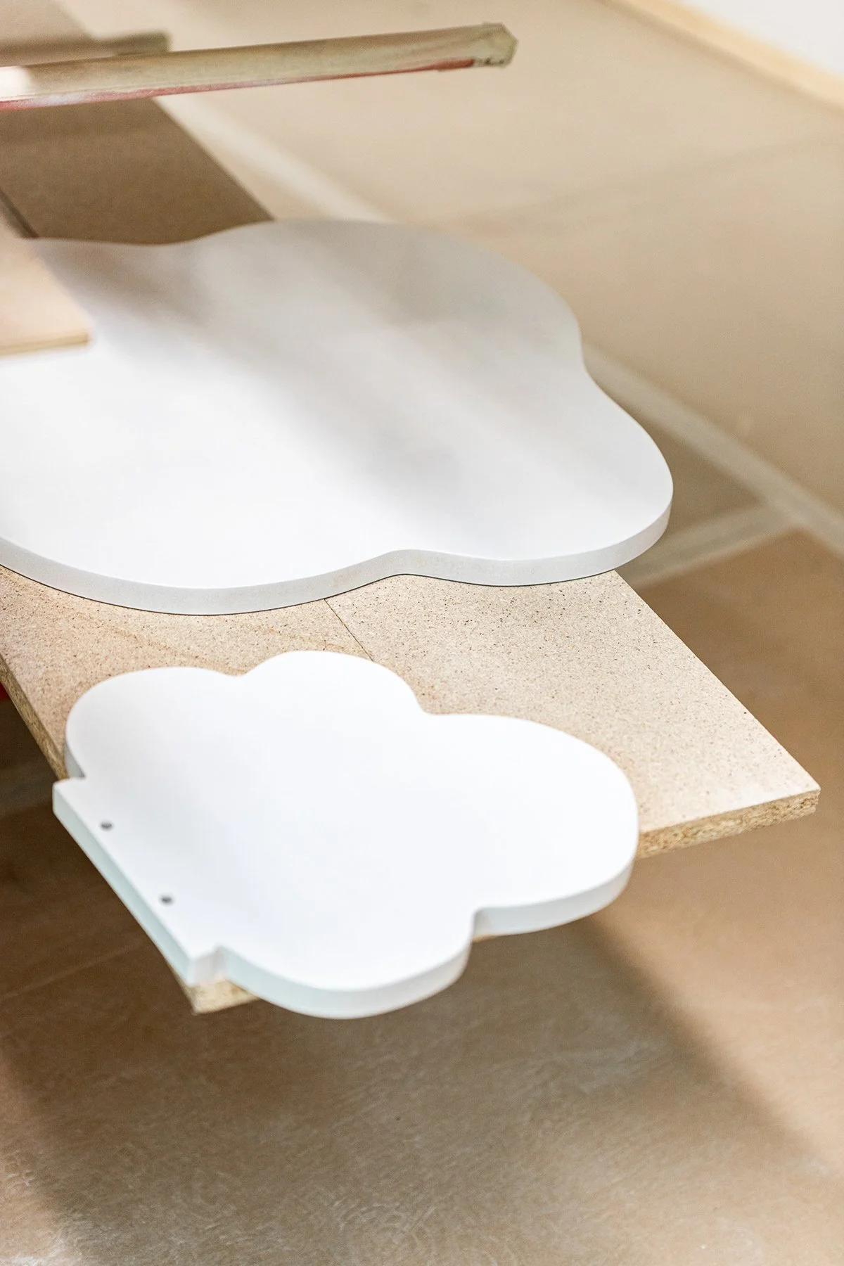 Deux étagères en forme de nuage, blanches, fixées l'une au-dessus de l'autre, sur un plan en bois, dans un intérieur.