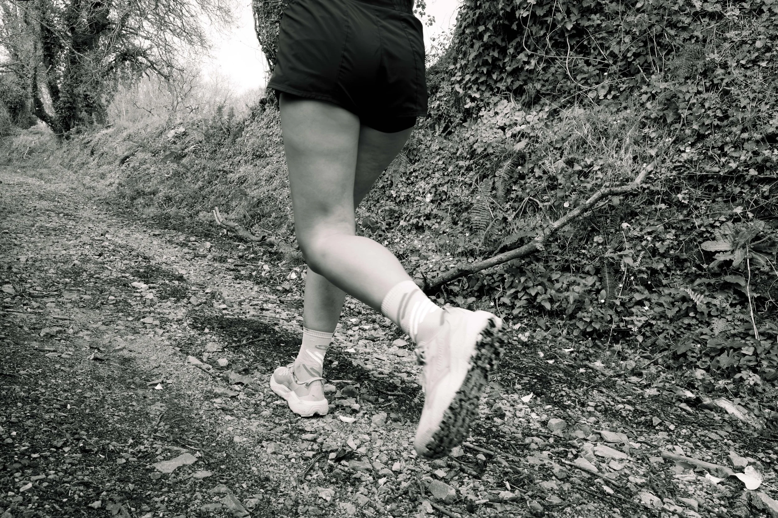 Une personne en leggings et chaussures de course haltère dans un sentier forestier, vue de derrière.