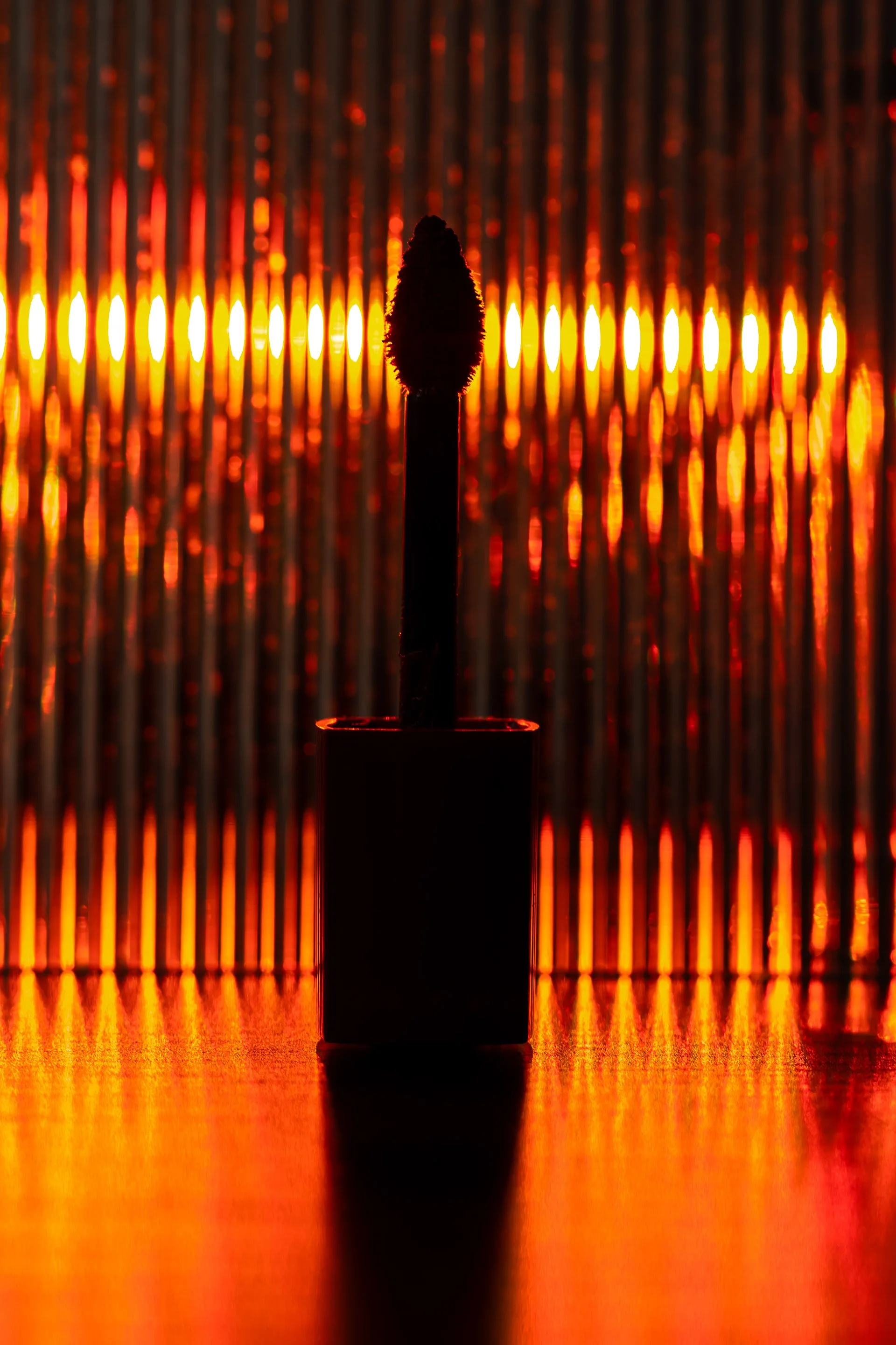 Une allumette allumée, vue de profil, avec une flamme rougeoyante derrière, créant un effet de silhouette contre des lumières rouges et orange.