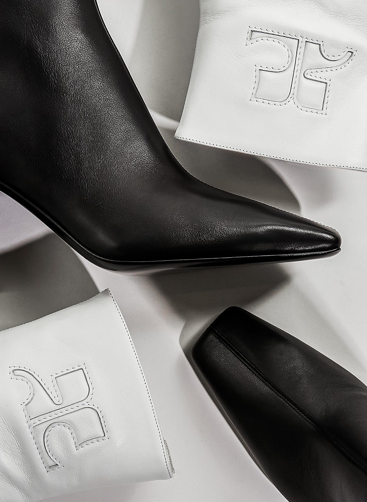 Chaussure noire pointue en cuir avec une semelle noire, deux sacs blancs avec une broderie en forme de logo, et un sac noir en cuir, tous placés sur un fond blanc.