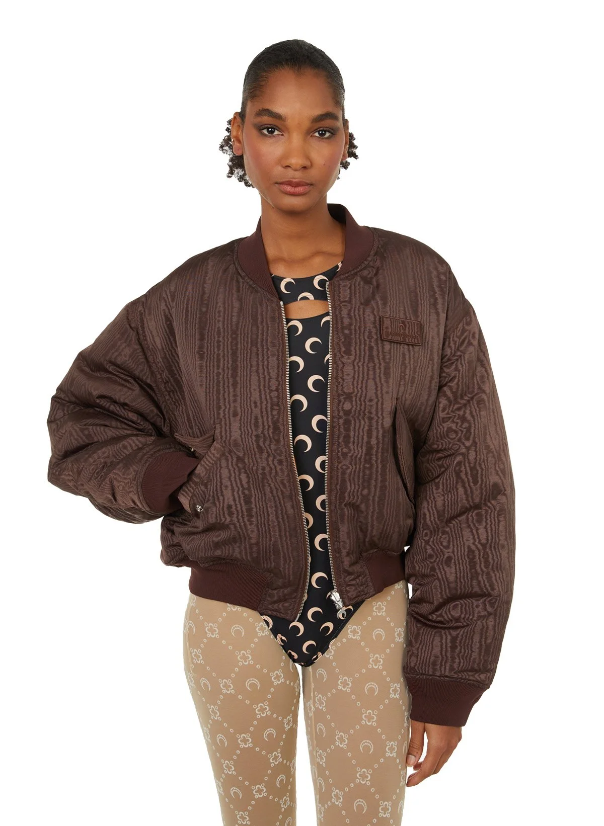 Femme portant une veste marron, une robe noire avec des motifs de lunes et un pantalon beige avec des motifs de cercles.