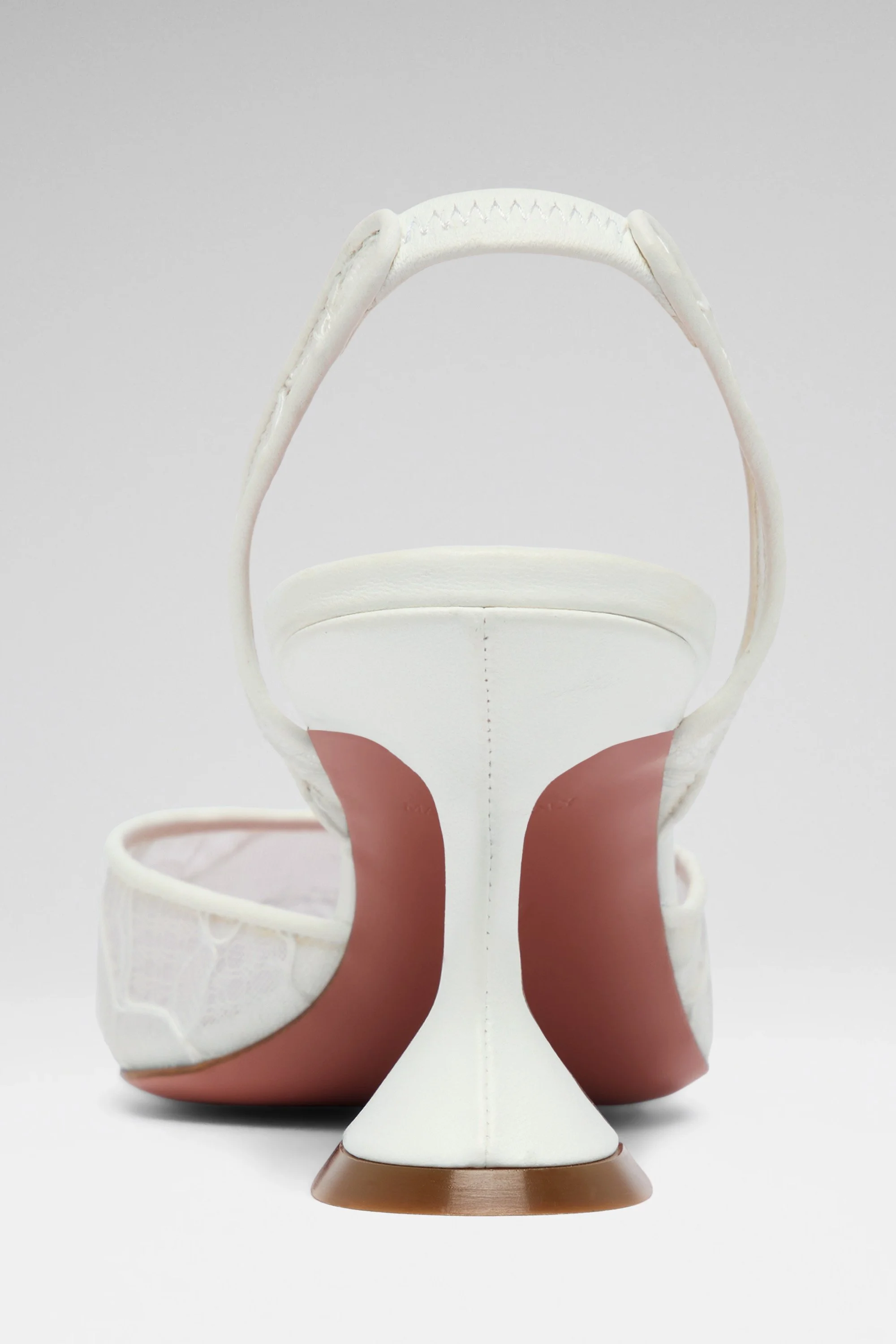 Une chaussure à talon blanche avec une semelle en caoutchouc rouge et une assise beige, vue de derrière contre un fond blanc.