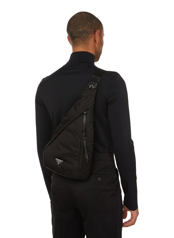 Un homme vu de dos portant un sac à bandoulière noir sur l'épaule droite, habillé en vêtements noirs.