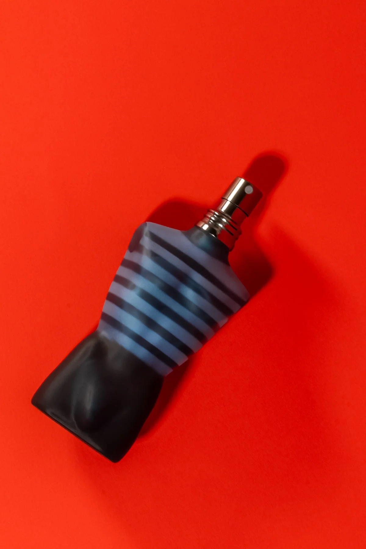 Un flacon de parfum noir et gris avec un motif rayé bleu et noir, placé sur un fond rouge