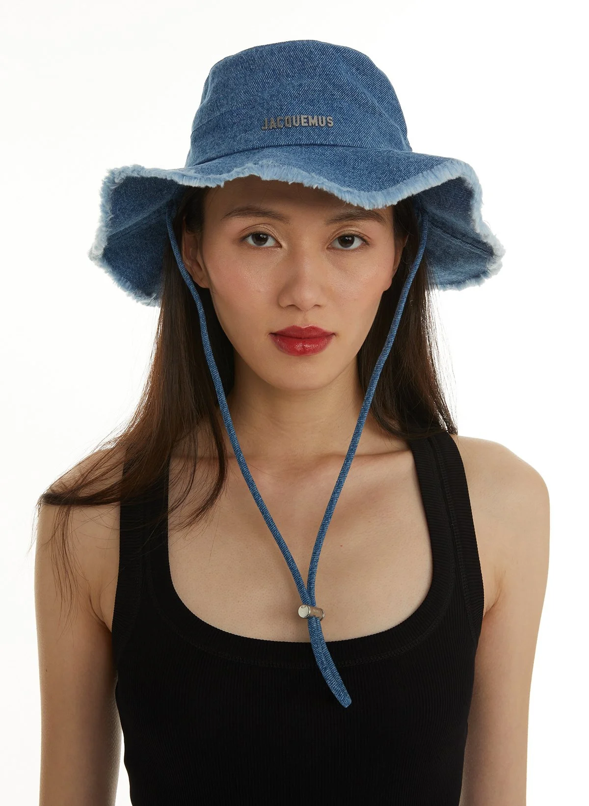 Jeune femme portant un chapeau bleu en denim avec bordure en tissu blanc, et un haut noir sans manches sur fond blanc.