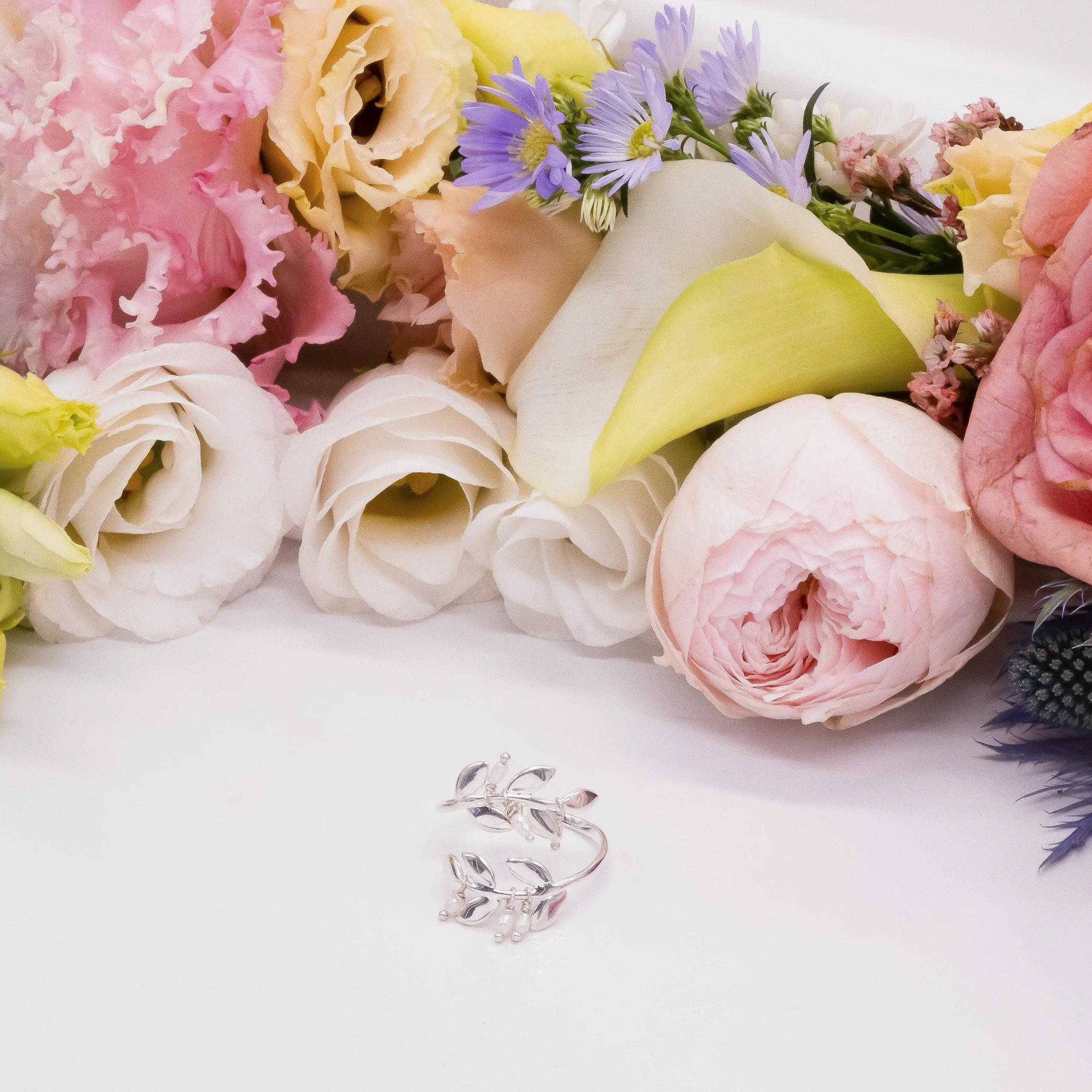 Un bouquet de fleurs pastel avec un anneau en argent en forme de branche de feuilles.