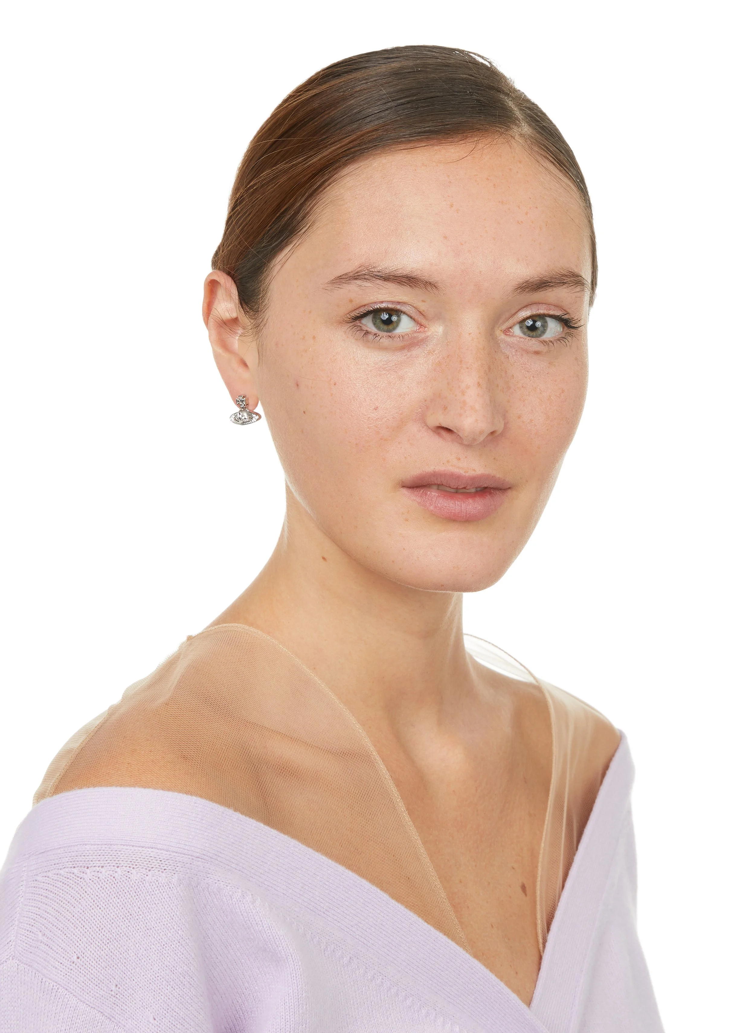 Jeune femme avec des cheveux bruns, peau claire, et yeux bleus, portant des boucles d'oreilles en argent et un pull violet clair, en gros plan avec un fond blanc.