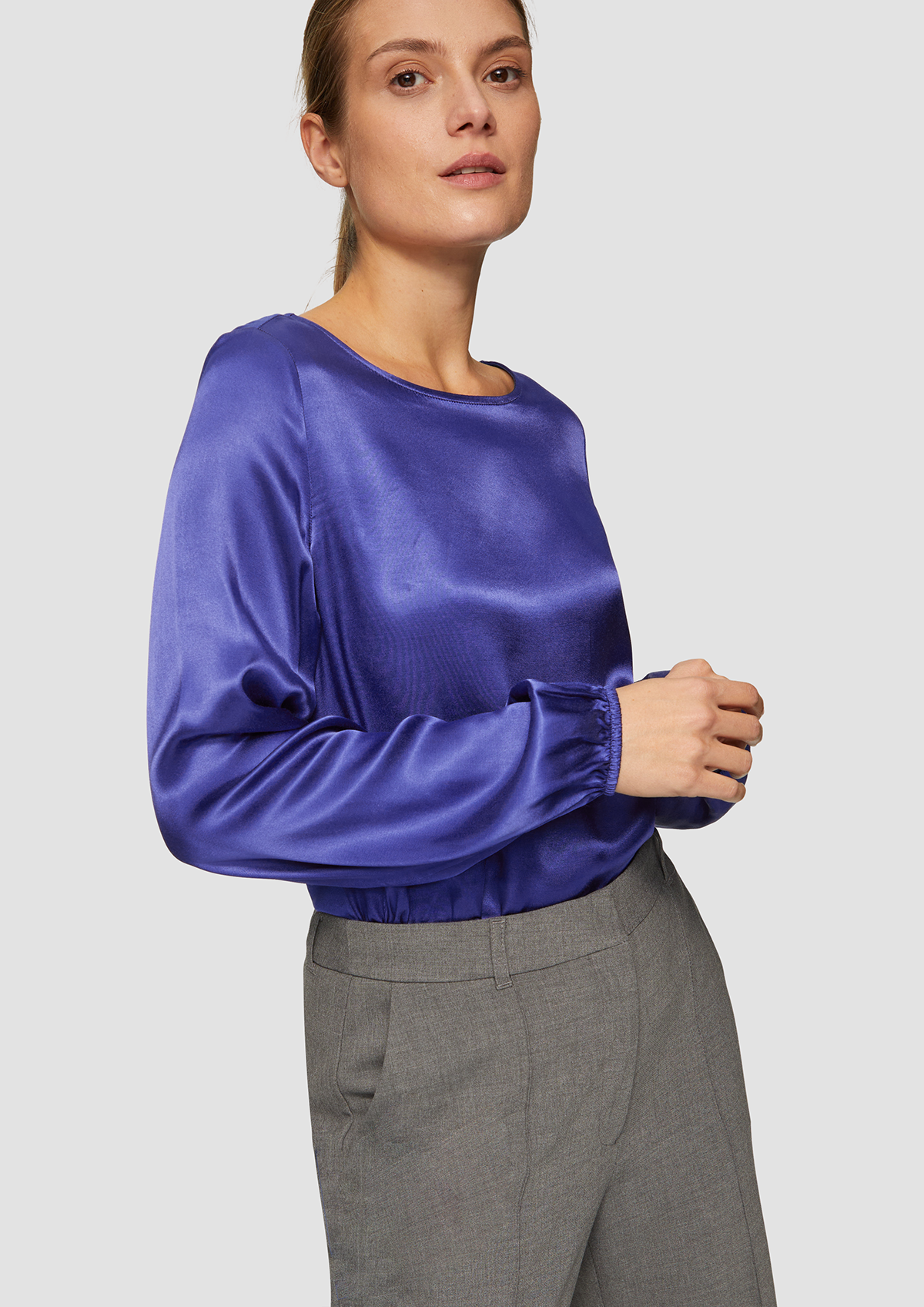 Femme portant un haut en satin bleu avec un pantalon gris.